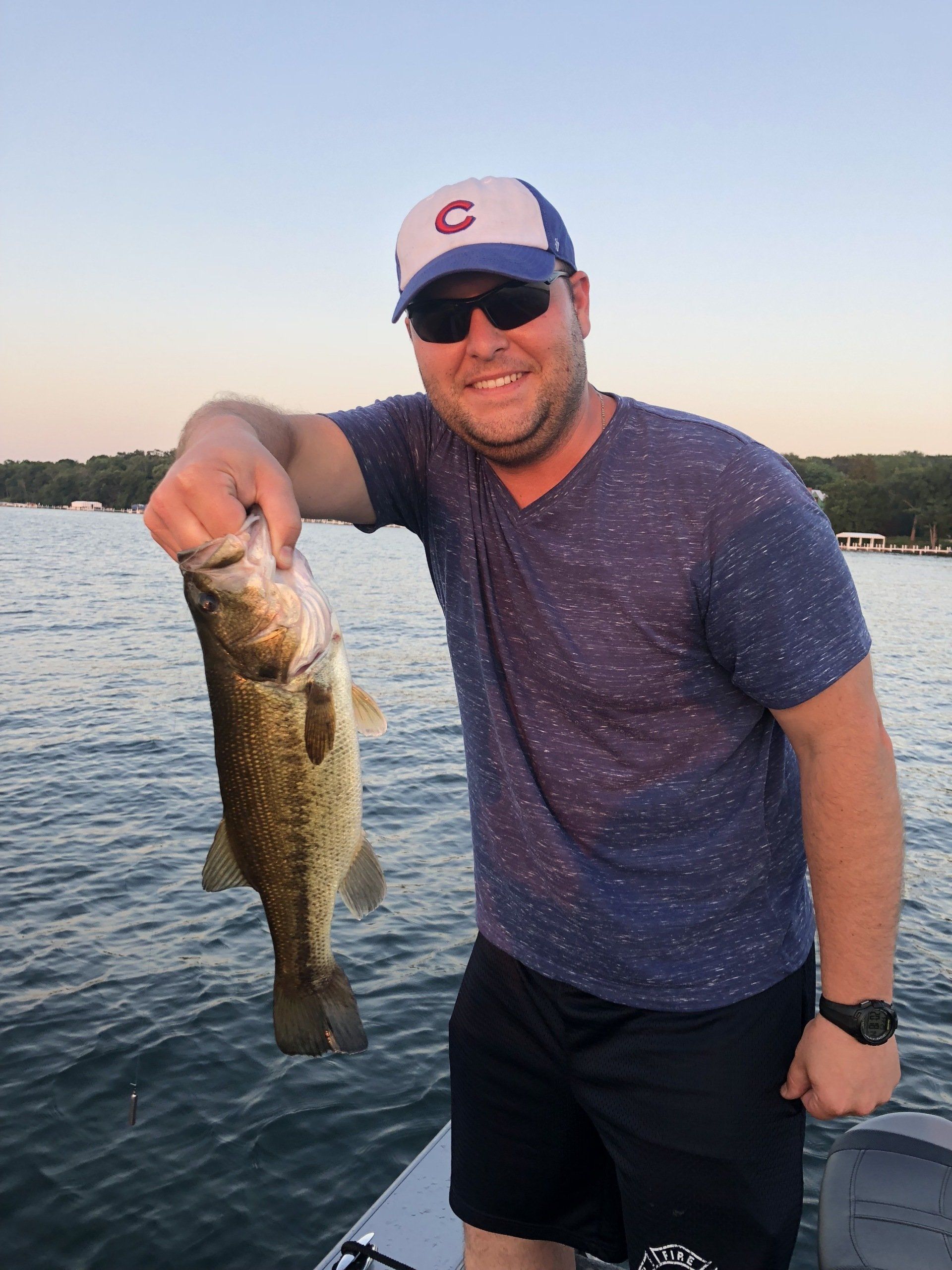 A man on a boat holding a fish with the letter c on his hat