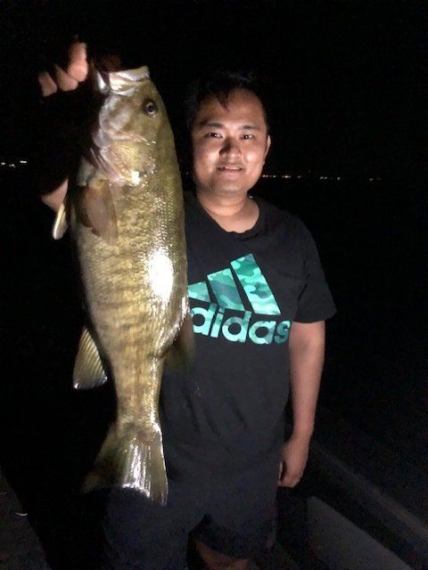 A man wearing an adidas shirt is holding a large fish