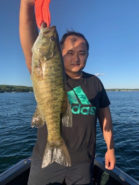 A man in an adidas shirt is holding a large fish