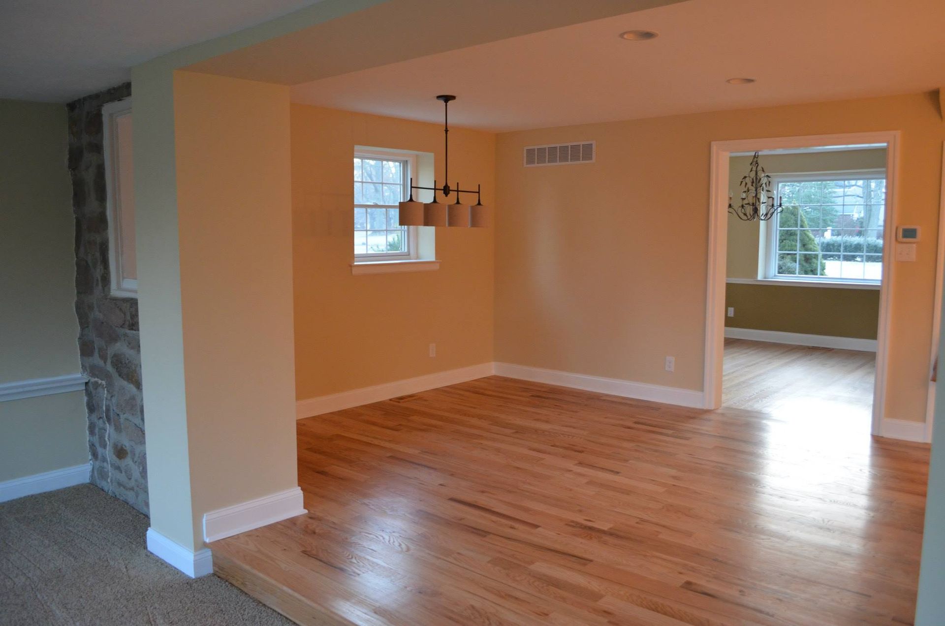 An empty living room with hardwood floors and a chandelier hanging from the ceiling.