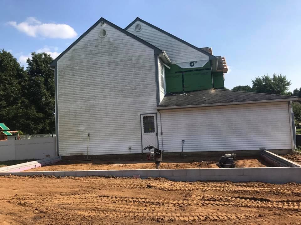 A white house with a green garage door is sitting on top of a dirt field.
