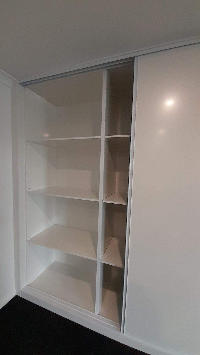 A white wardrobe with sliding doors and shelves in a room.