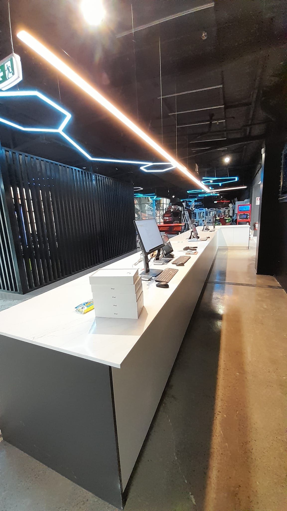 A long white table with a computer on it in a dark room.