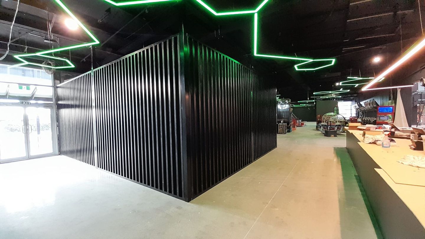 A large room with a black wall and green lights on the ceiling.