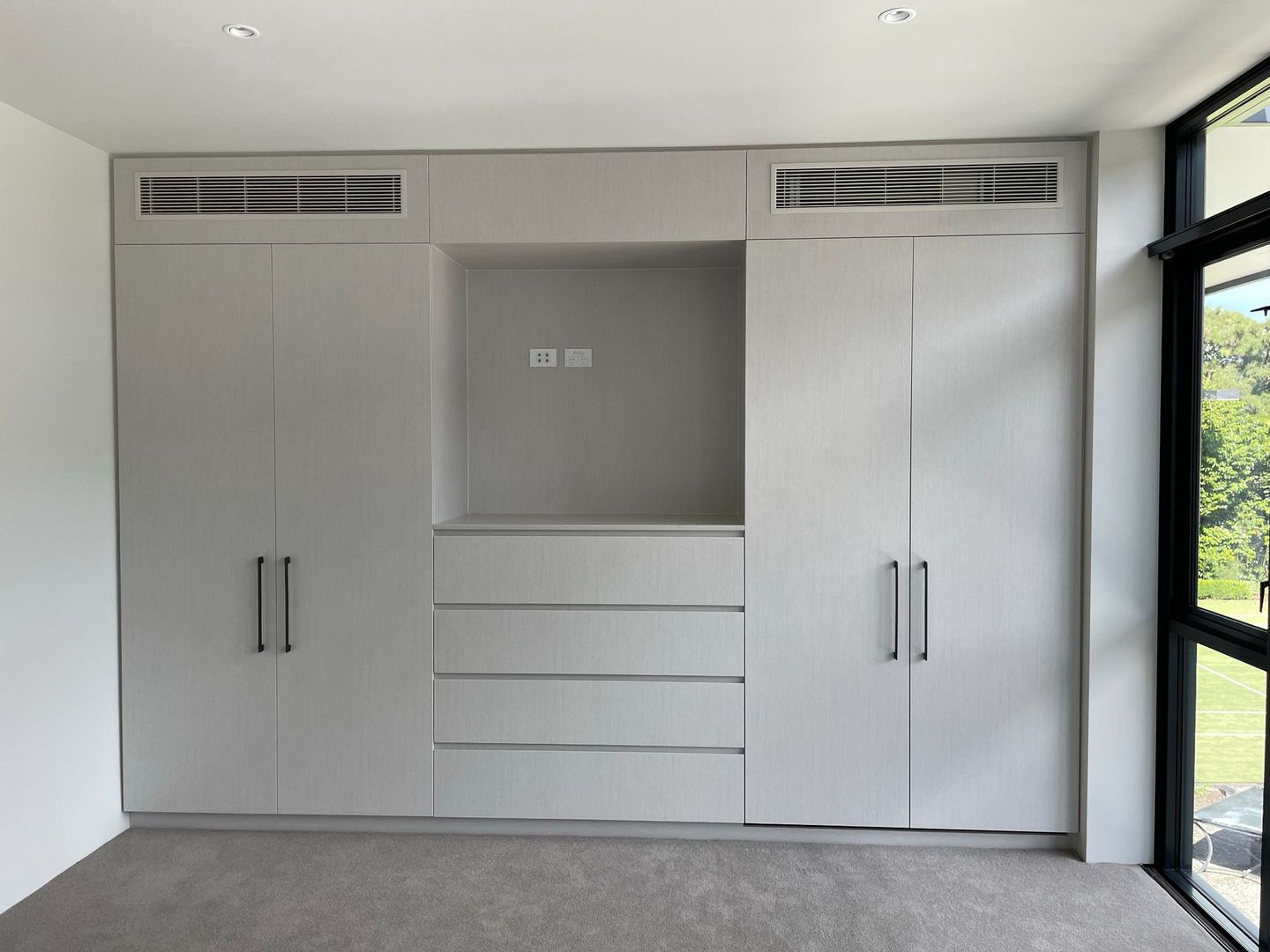 A bedroom with white cabinets and drawers and a large window.