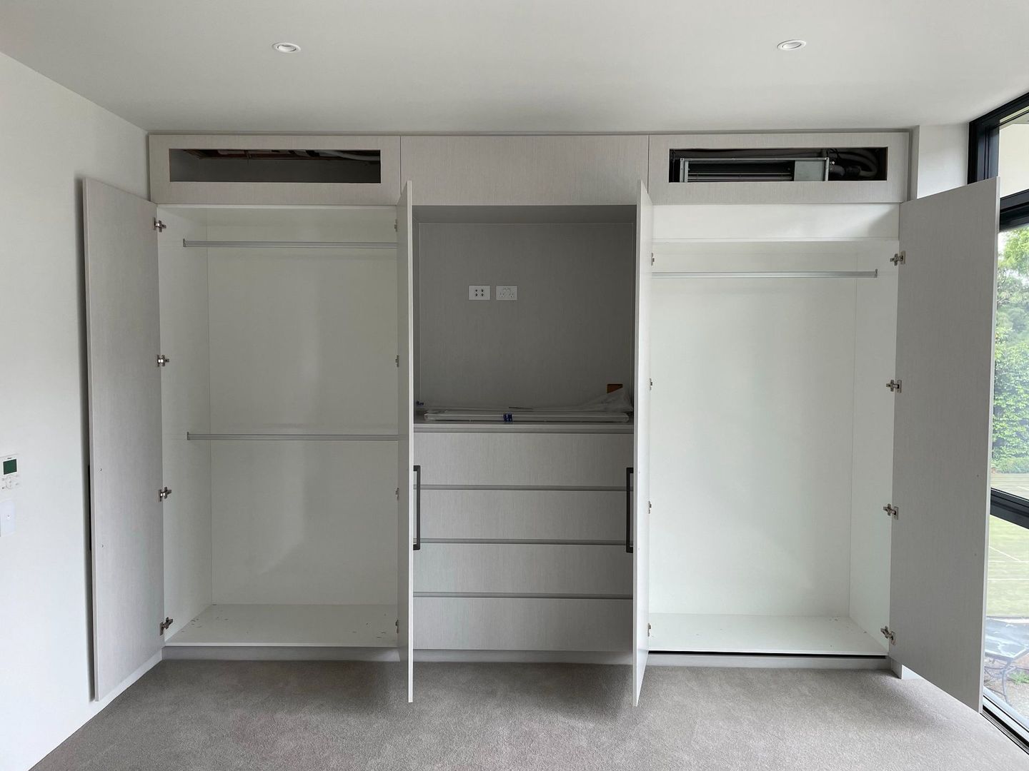 A bedroom with a large white wardrobe with the doors open.