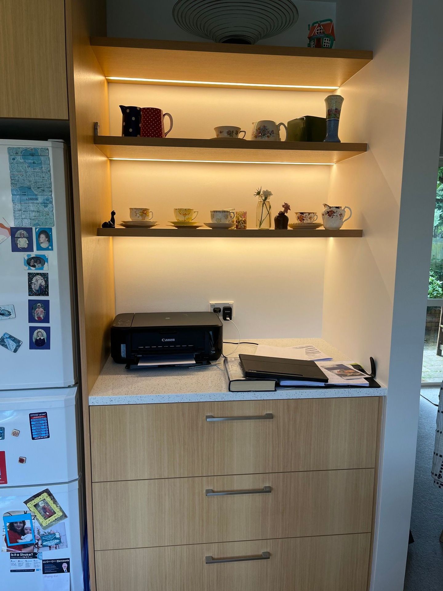 A printer is sitting on a counter in a kitchen next to a refrigerator.