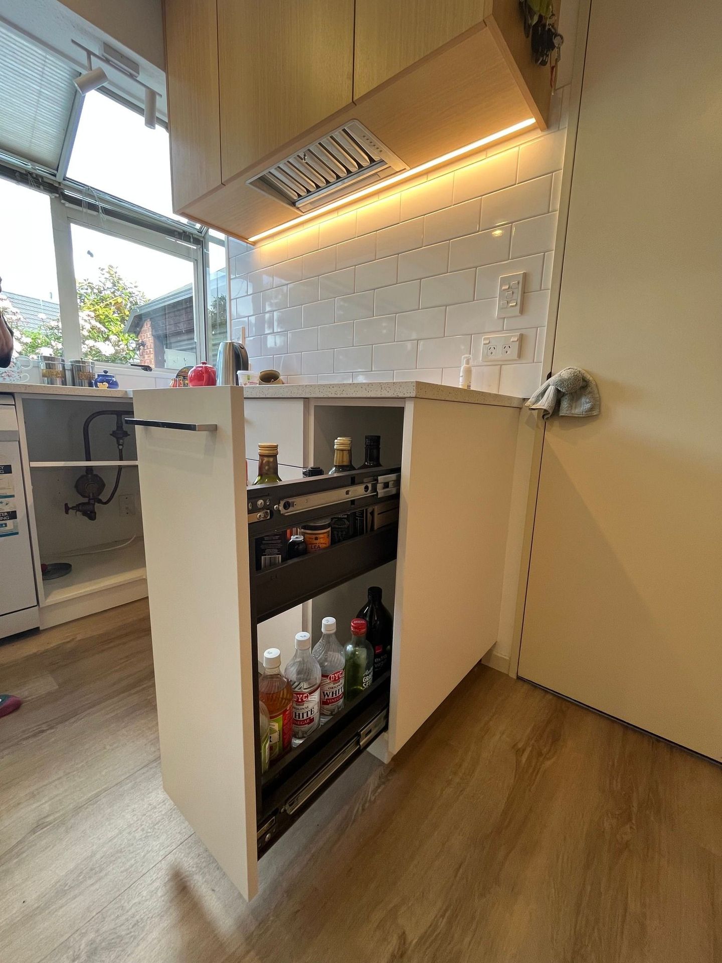 A kitchen with a pull out drawer filled with bottles.