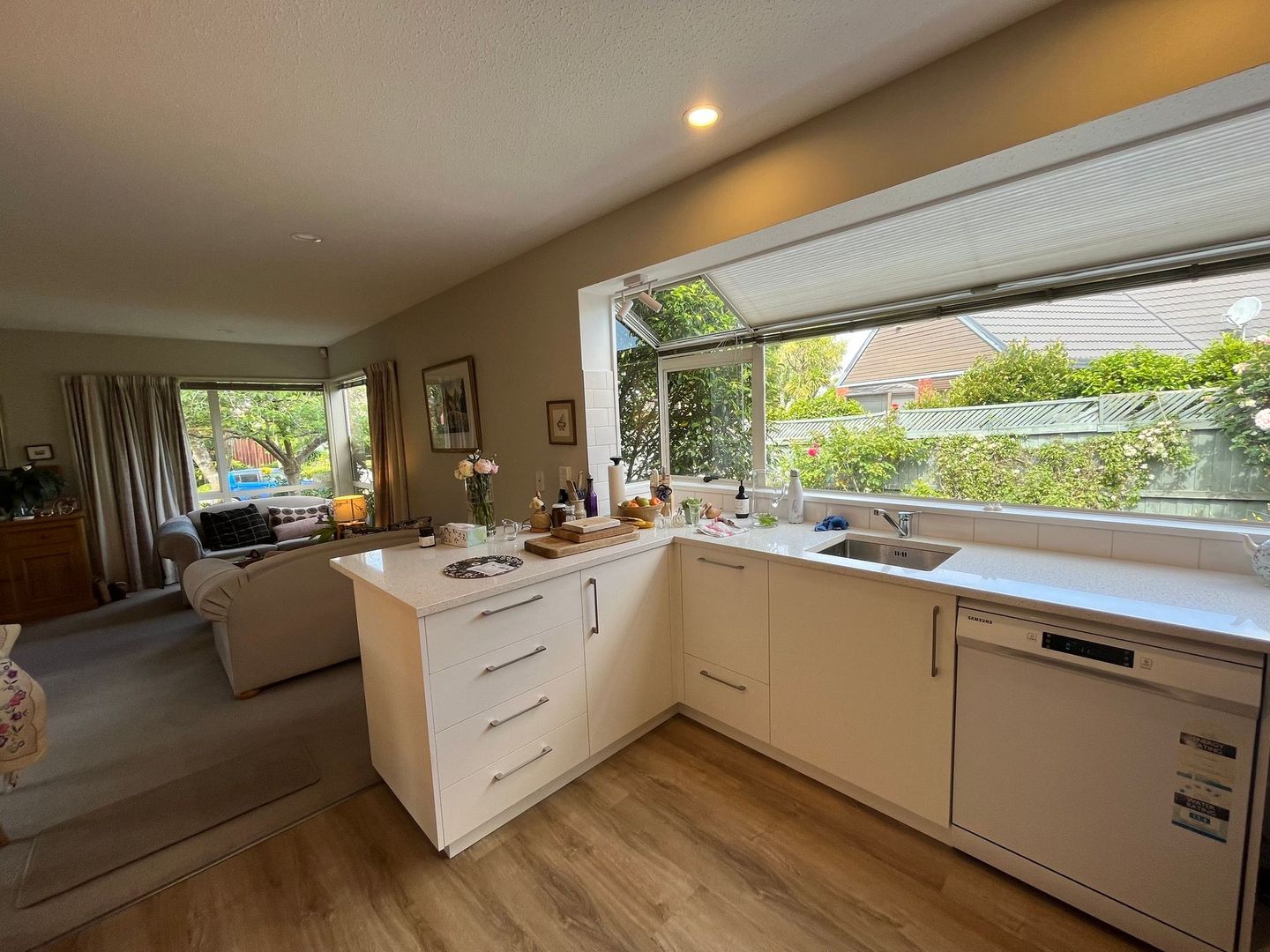 A kitchen with white cabinets , a sink , a dishwasher and a large window.