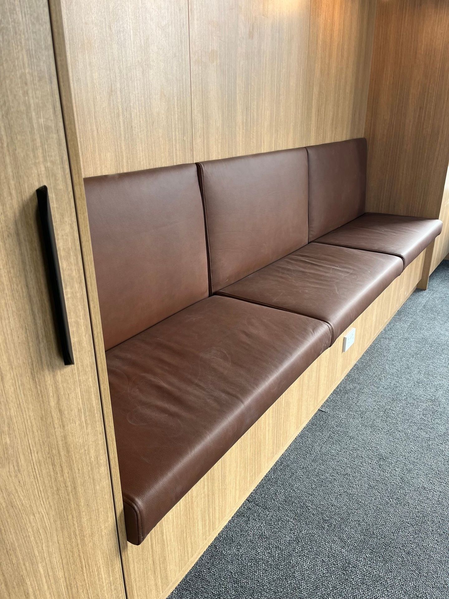 A brown leather couch is sitting next to a wooden wall.