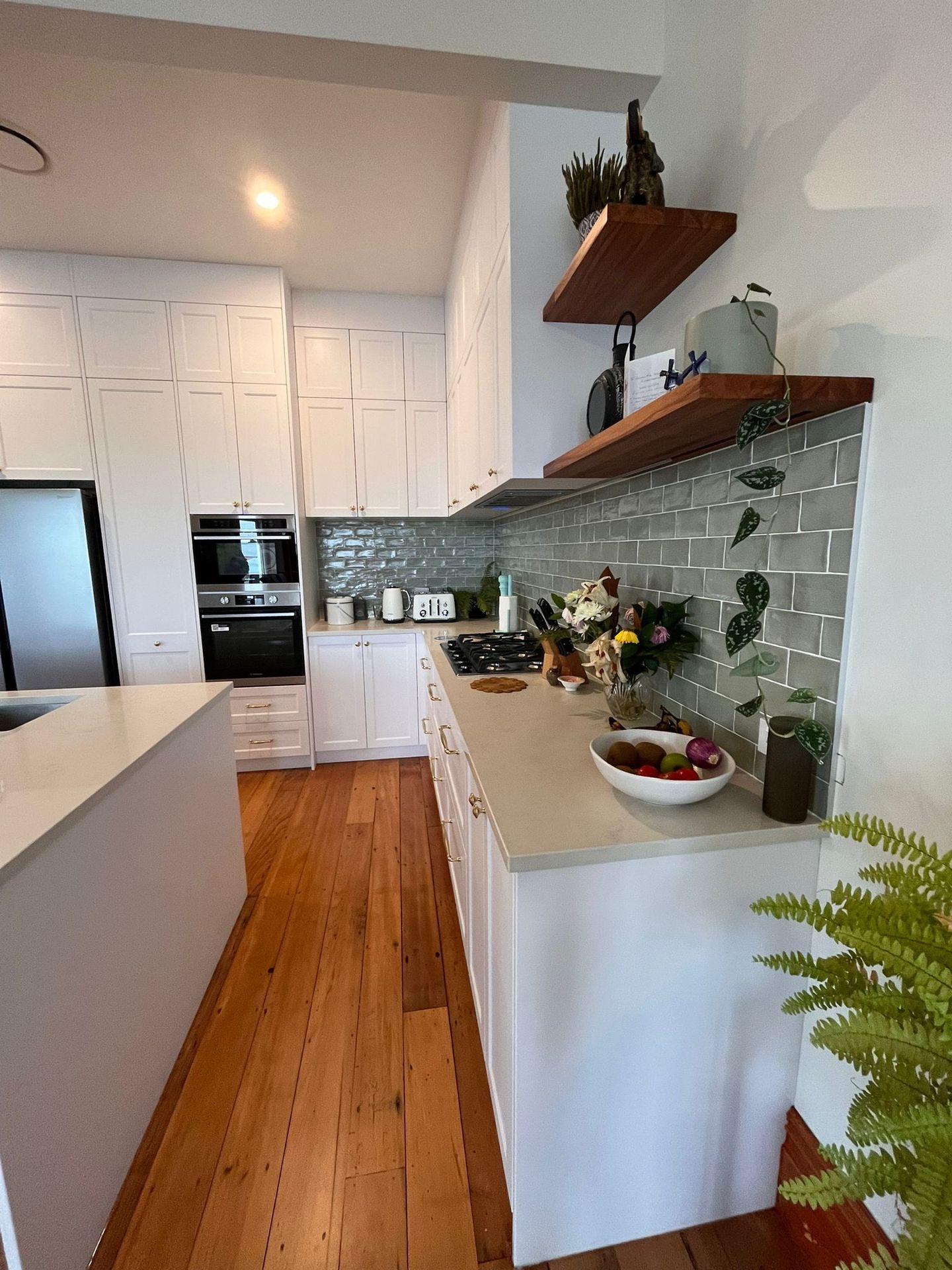 A kitchen with white cabinets and wooden floors and a stove top oven.