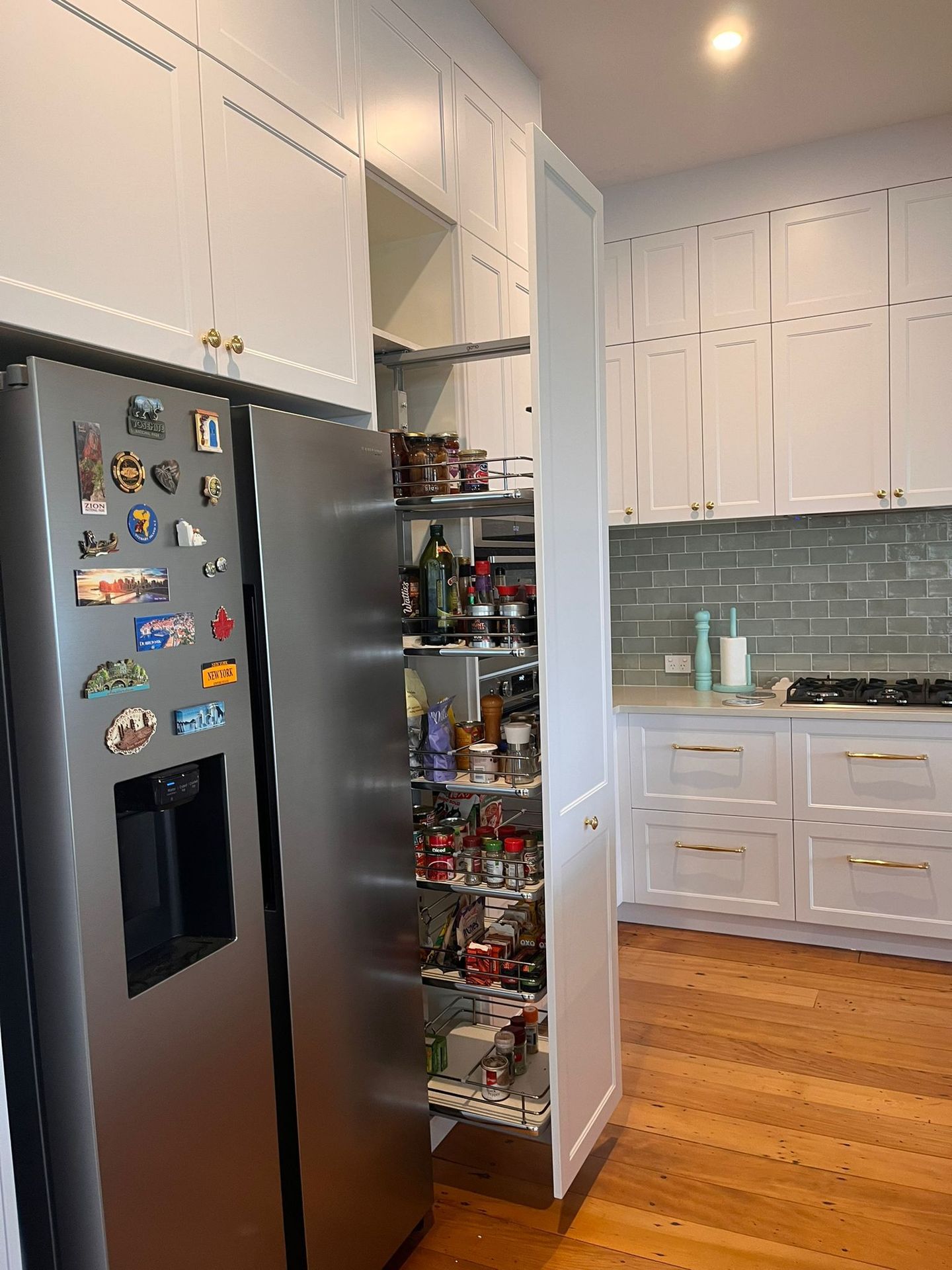 A kitchen with a stainless steel refrigerator and a pull out pantry.