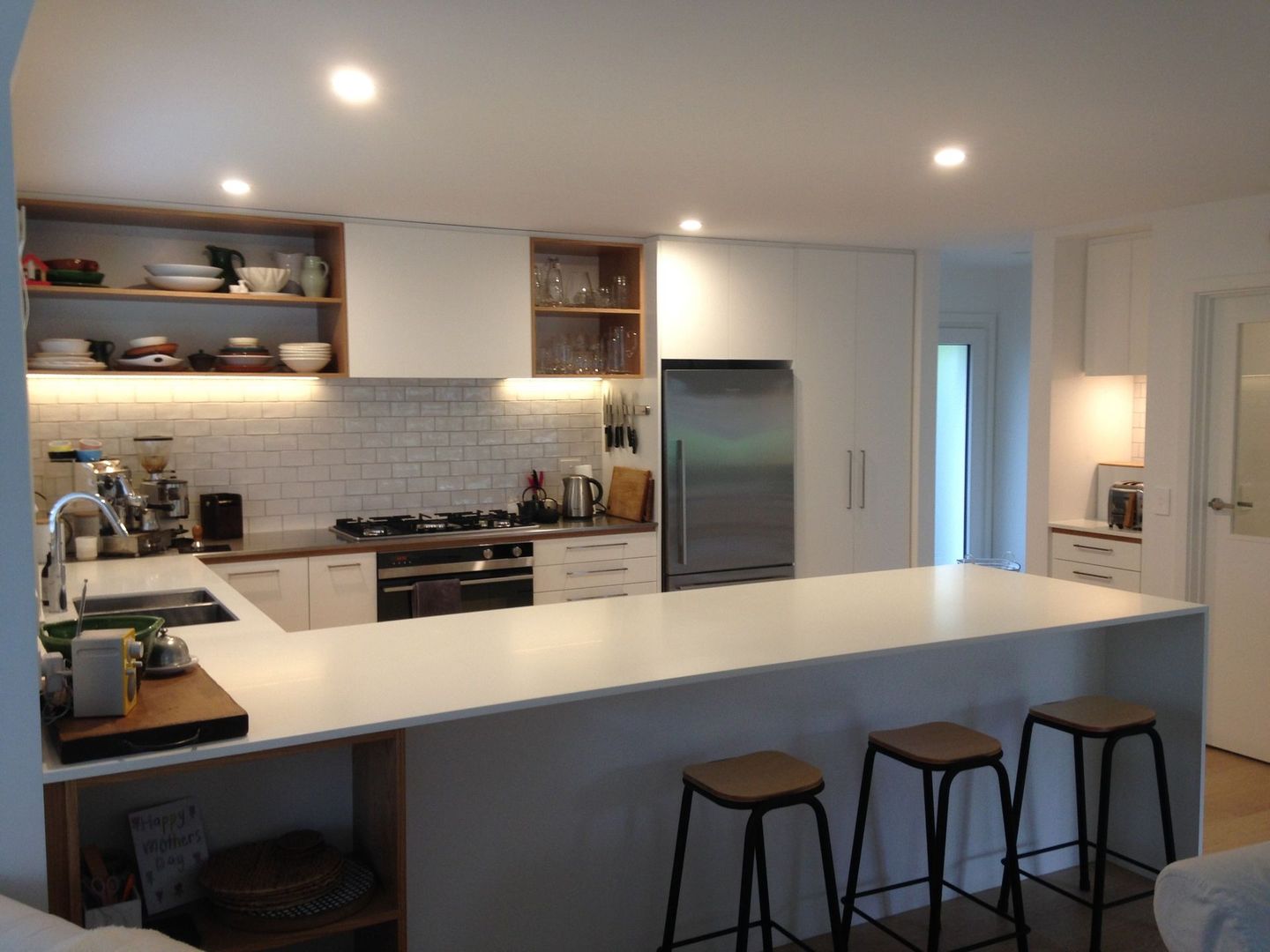 A kitchen with white cabinets , stools , a refrigerator and a stove.