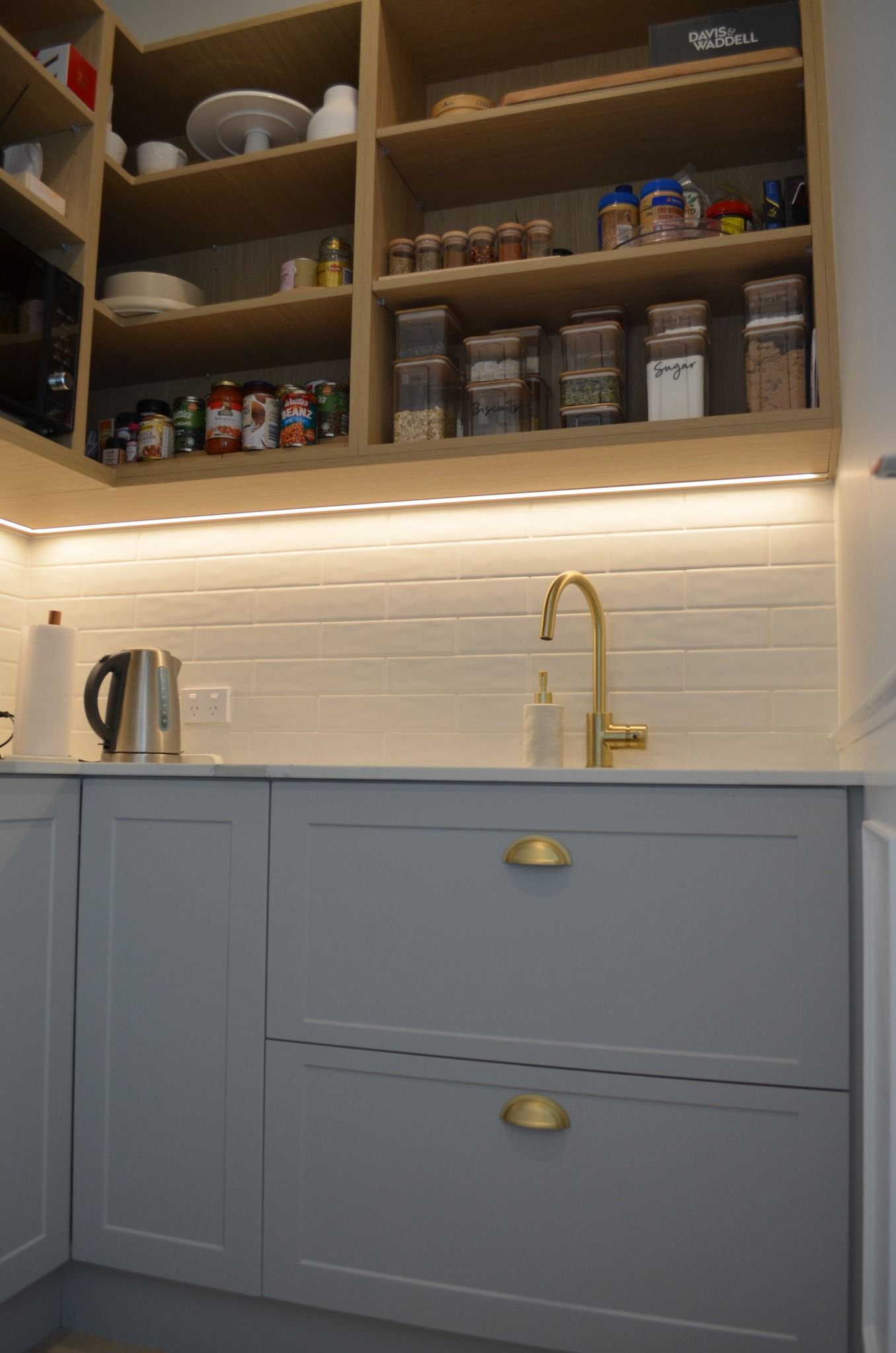 A kitchen with a sink , cabinets , shelves and a faucet.