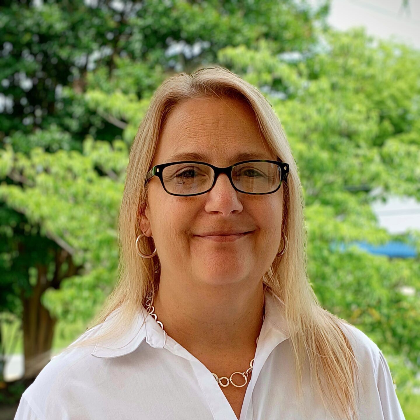 Woman wearing glasses and blazer, smiling. Against a blue background.