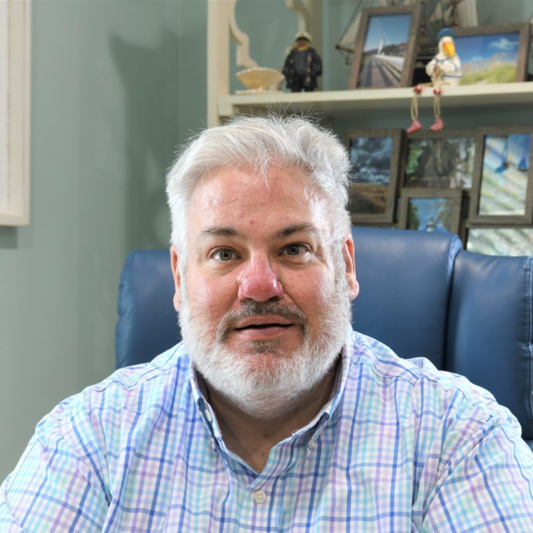 Woman wearing glasses and blazer, smiling. Against a blue background.
