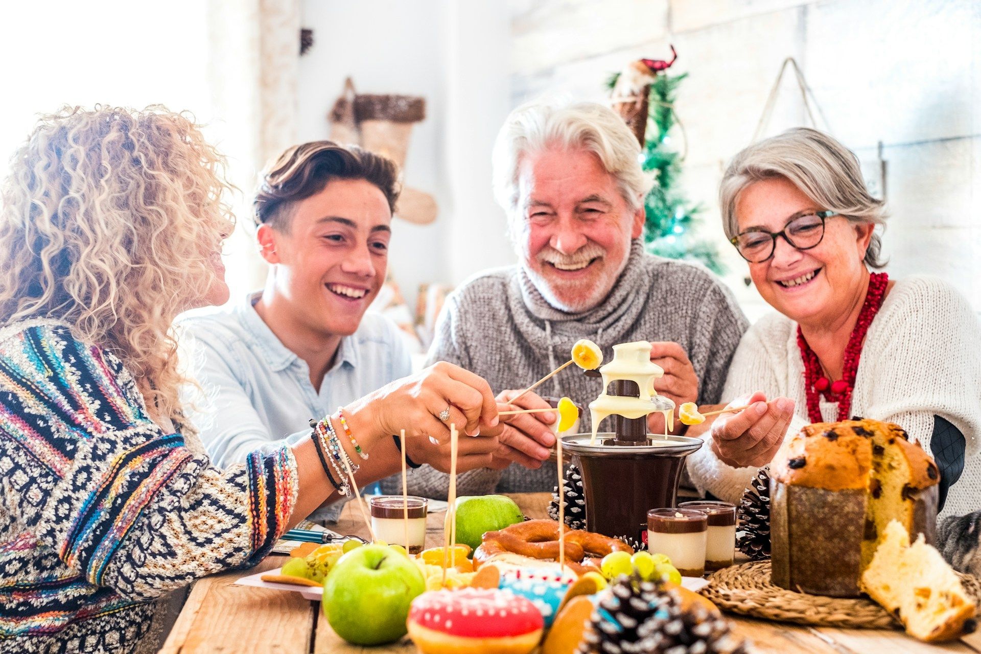 Family laughing, dipping fruit into a chocolate fountain, at a festive table.