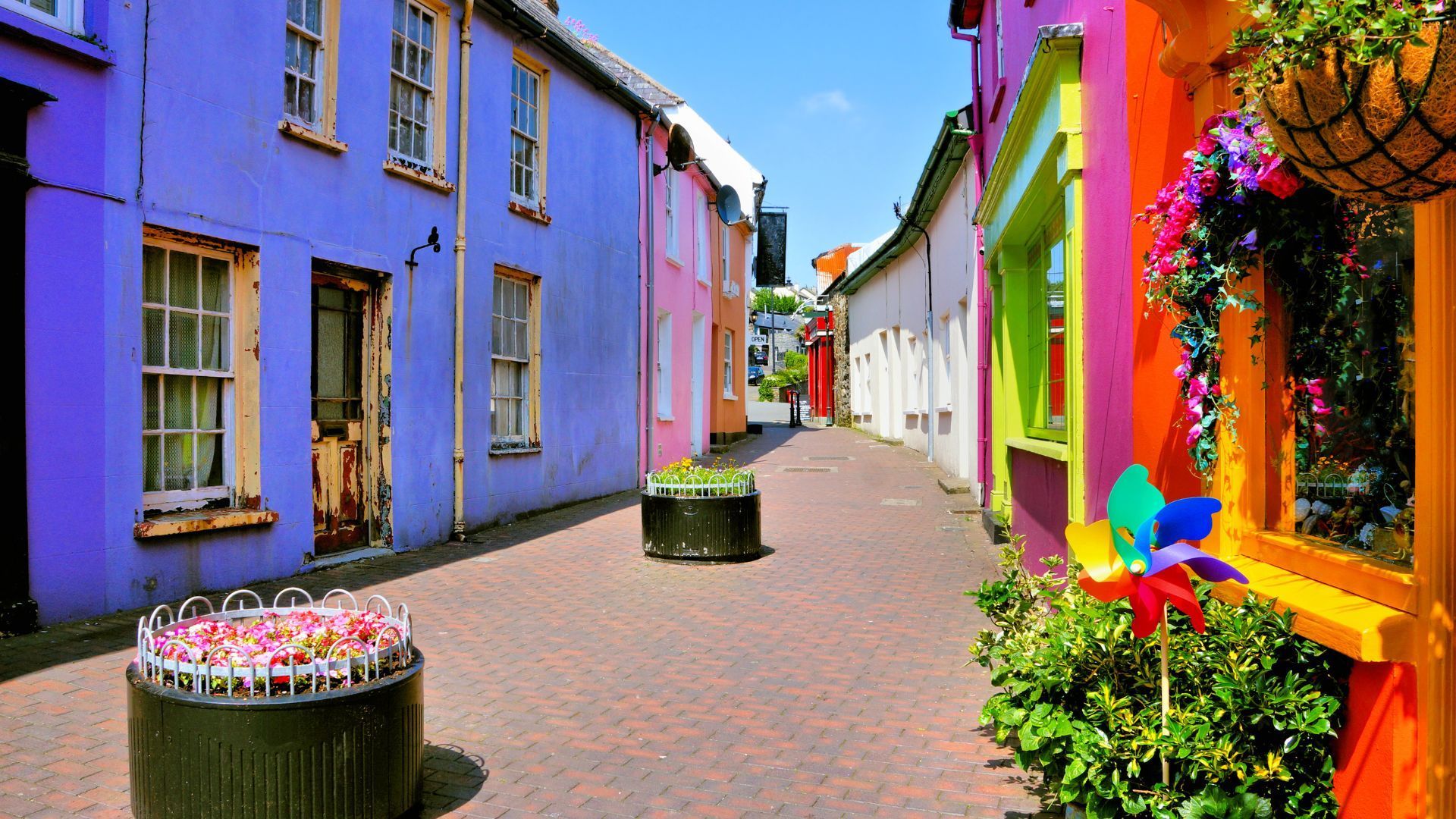 Colorful street with buildings painted purple, pink, and orange, with cobblestone pavement, and floral decorations.