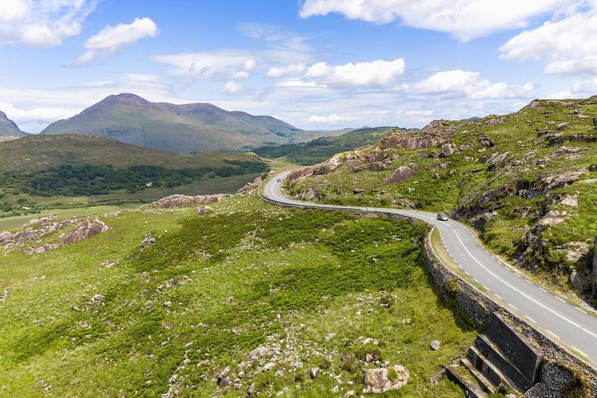 Winding mountain road through green hills under a bright blue sky with clouds