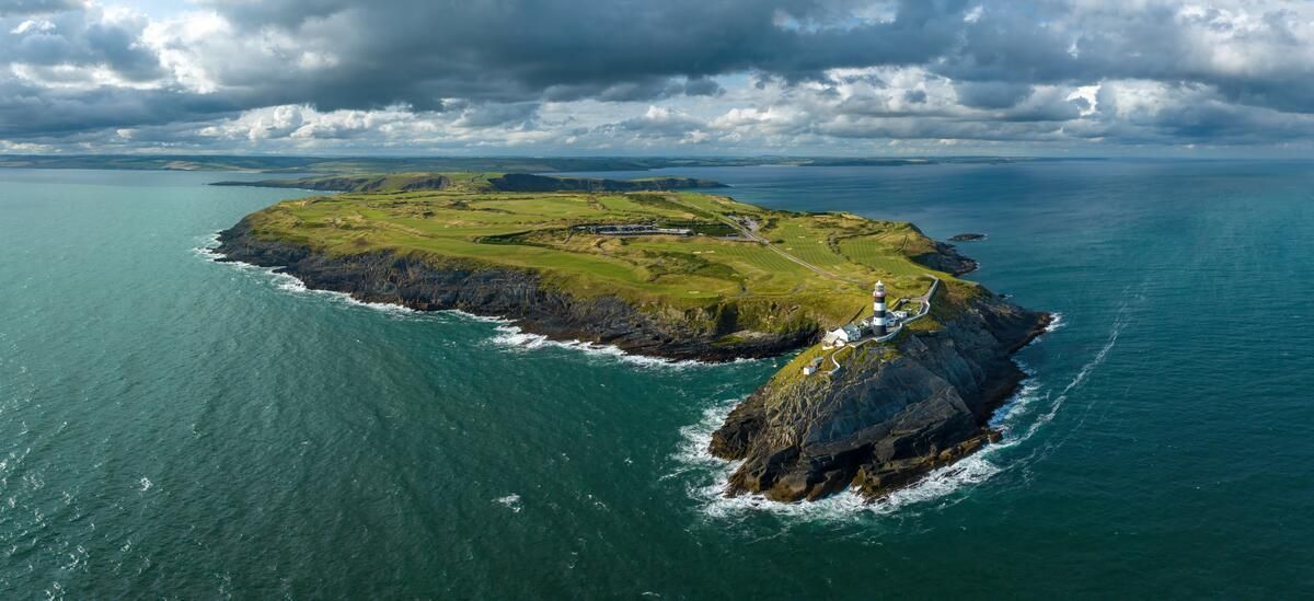 Aerial view of Kinsale Old Head with rocky shores in turquoise ocean under cloudy sky