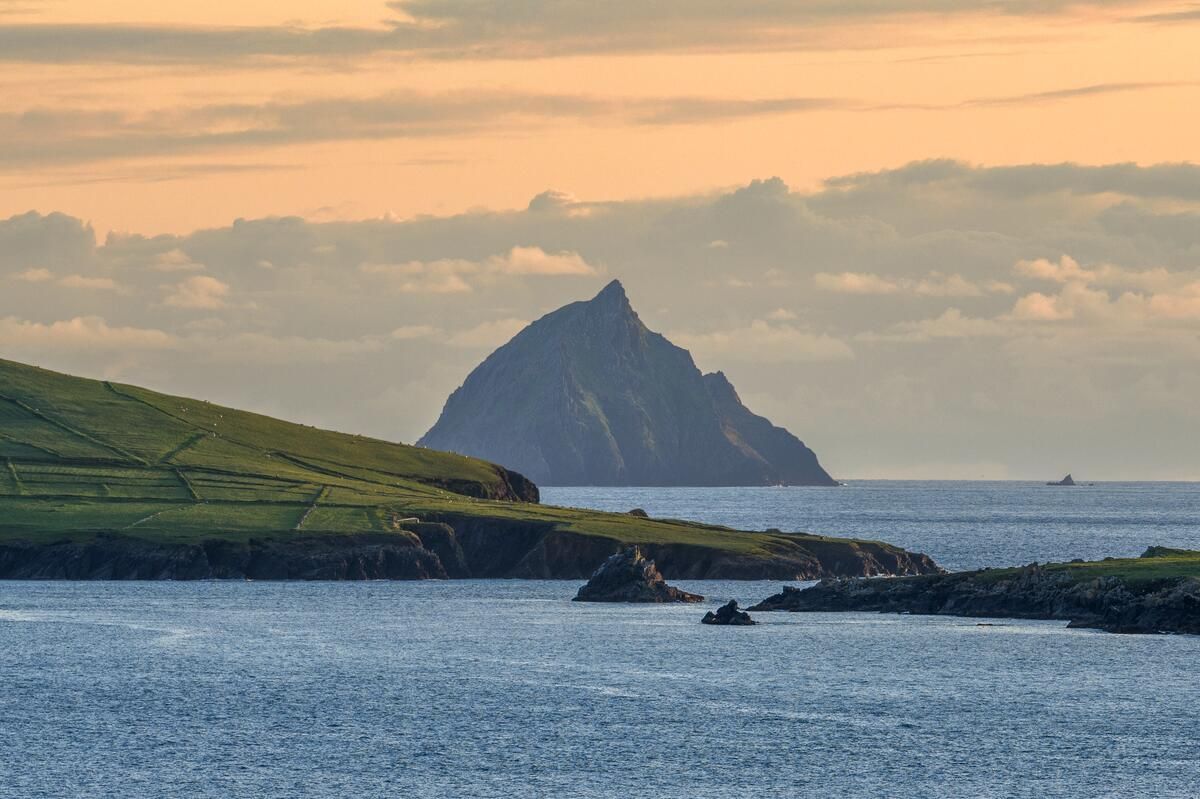 Rocky sea coast at sunset with a sharp island peak in the distance and calm blue water