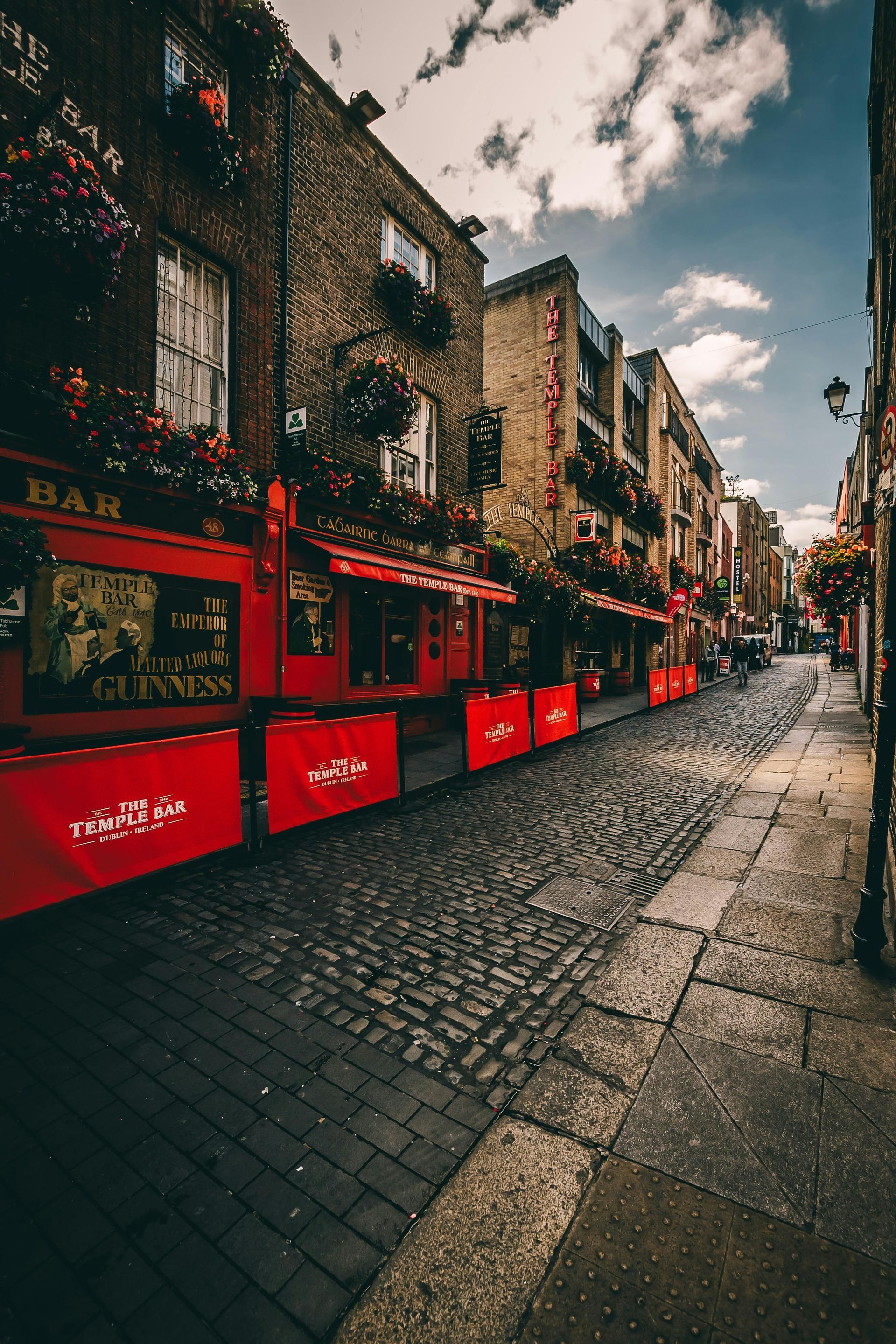 Red pub exterior on a cobblestone street in a European city with floral window boxes.