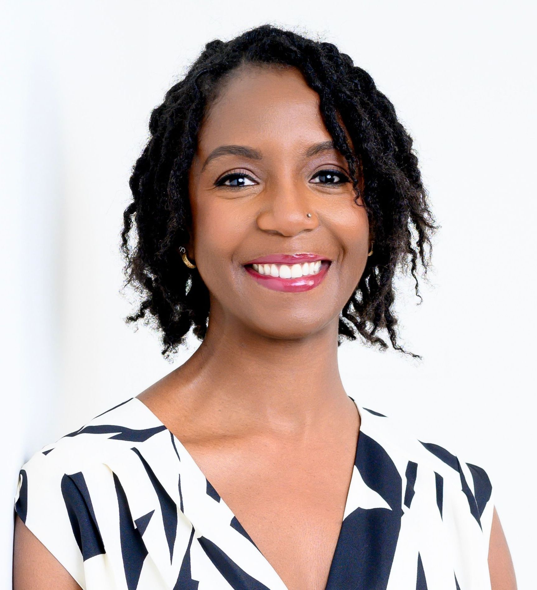 Woman with dark hair in a patterned dress smiling at the camera against a bright white background.