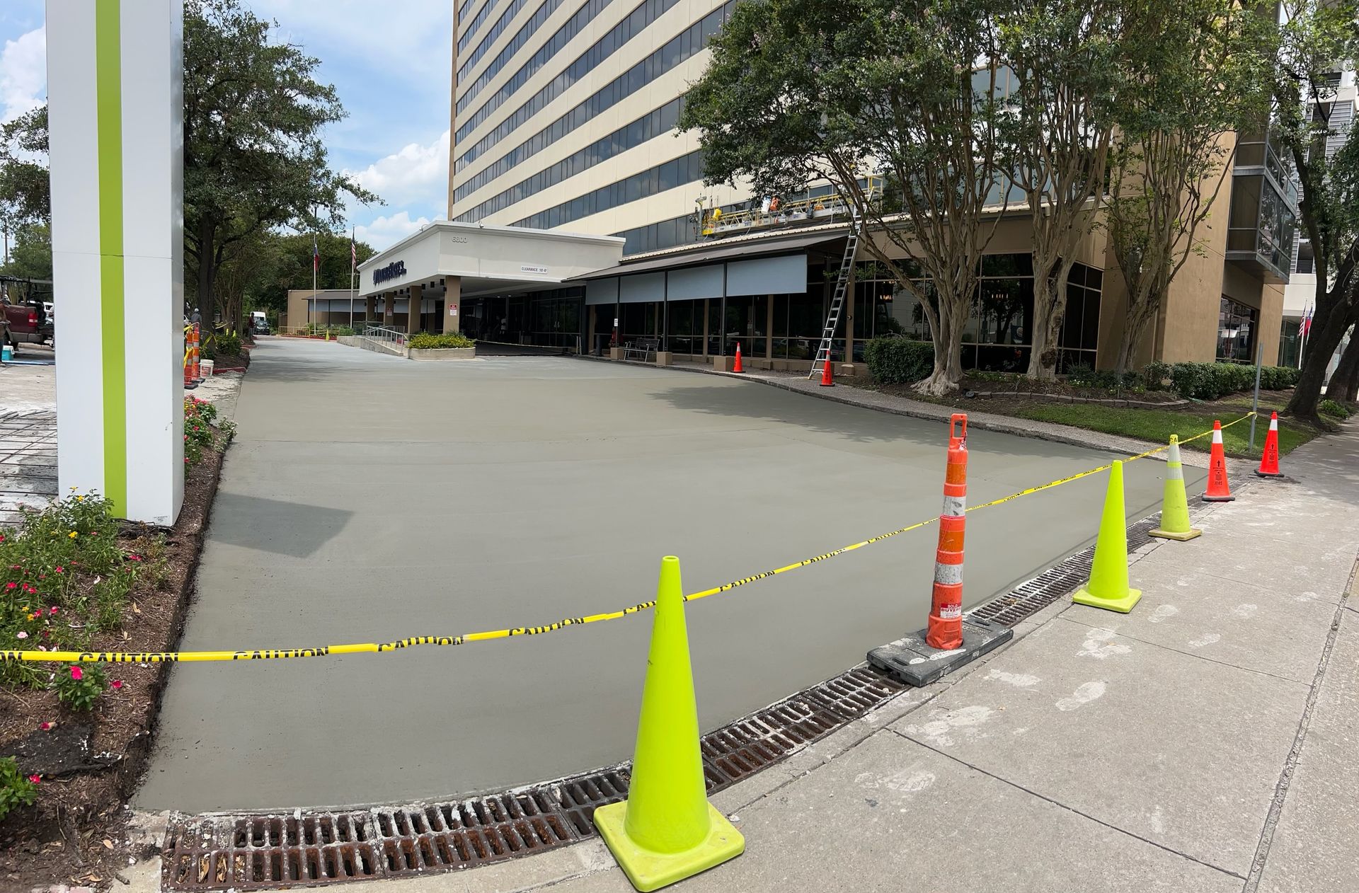 Freshly poured concrete driveway in front of a building, marked with cones and caution tape.