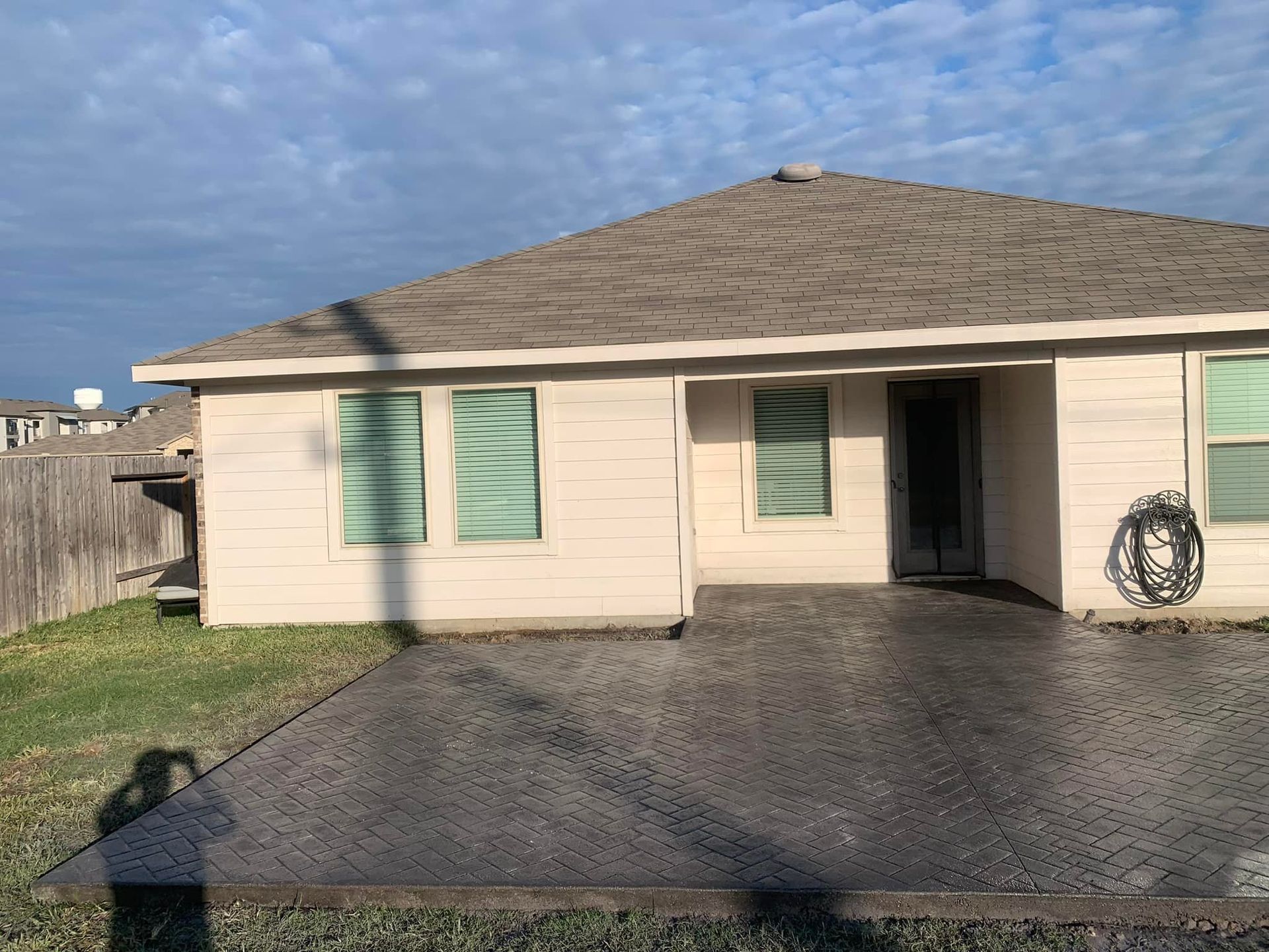 Tan house with a dark gray concrete patio and a cloudy sky.