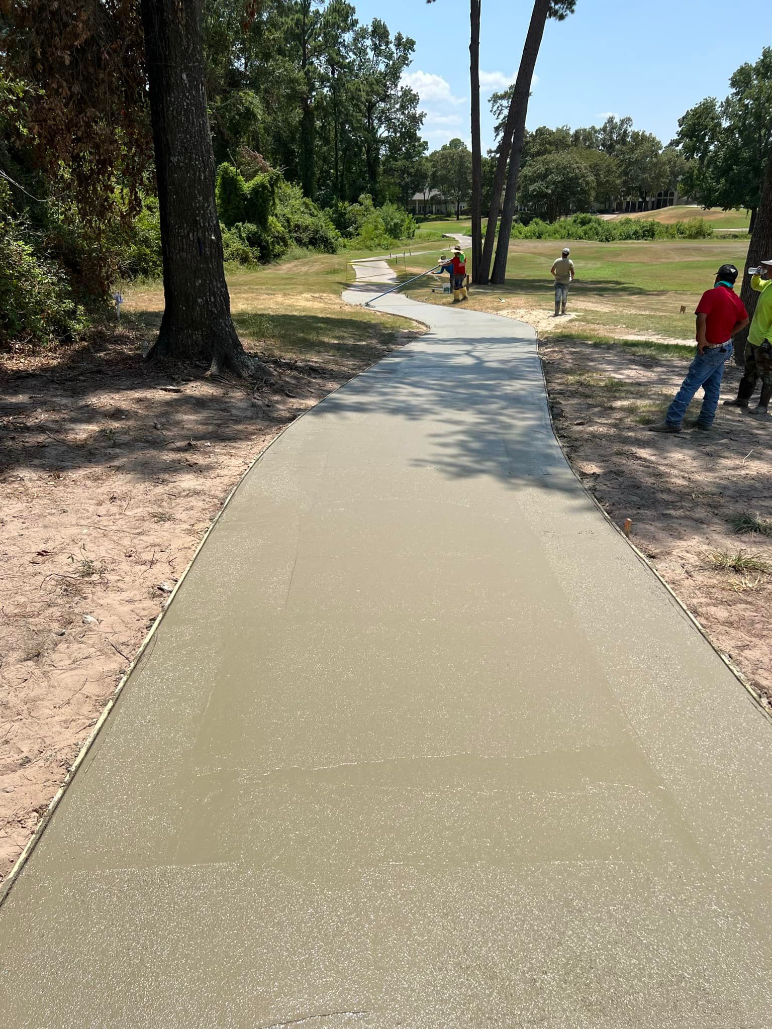 Newly poured concrete walkway with workers nearby; sunny outdoor setting.