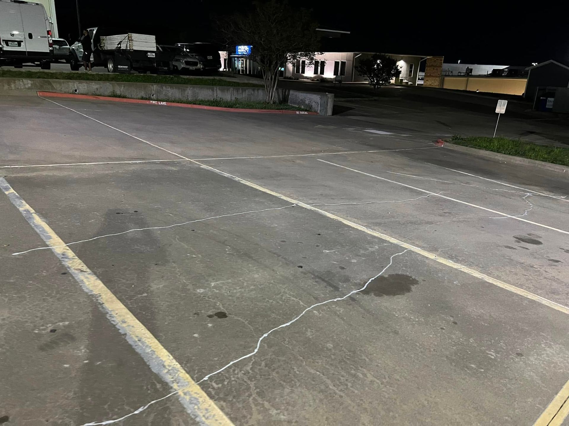 Parking lot at night with painted lines and parked vehicles.
