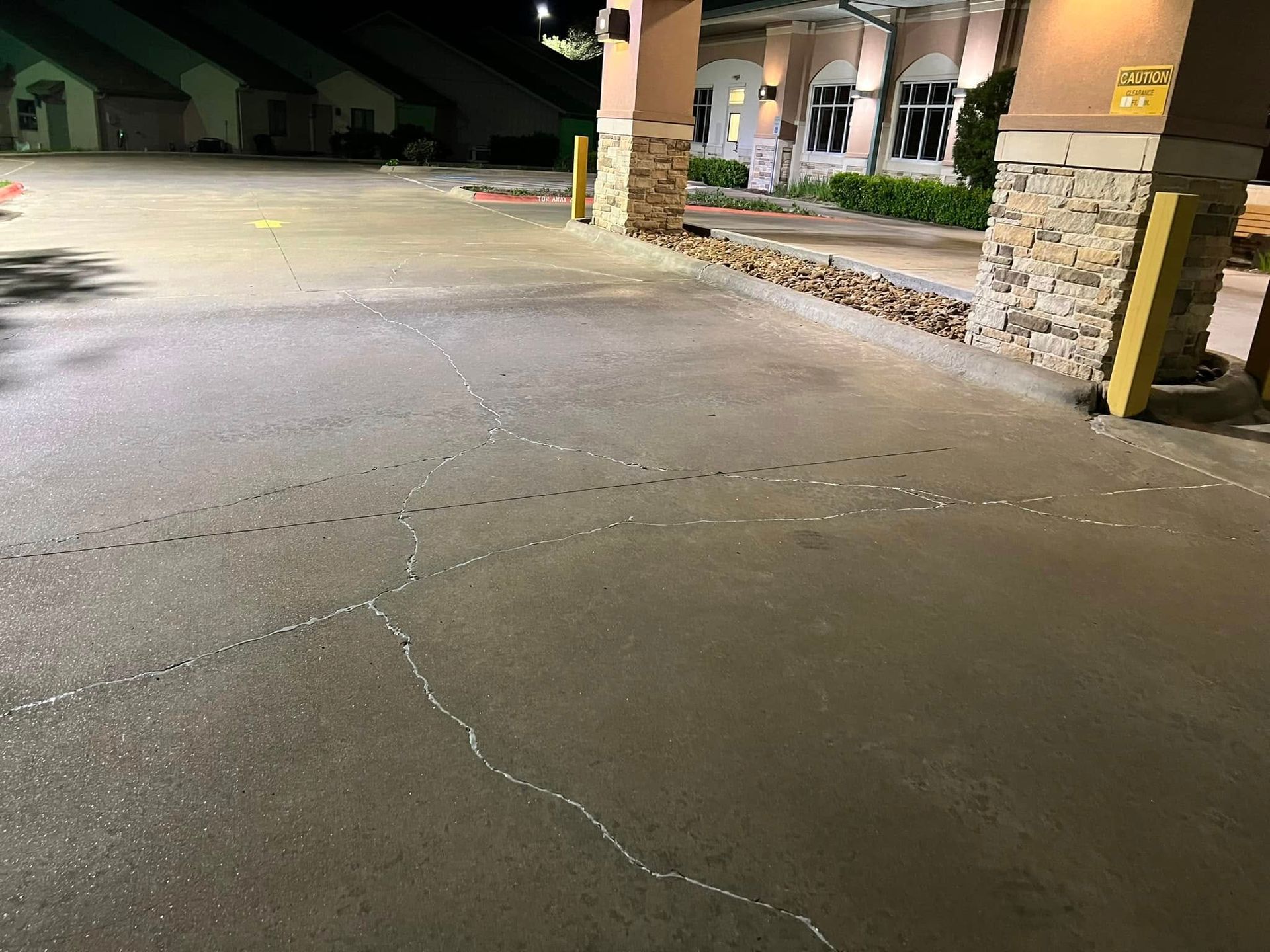 Concrete driveway with white sealant lines in front of a building with stone columns.