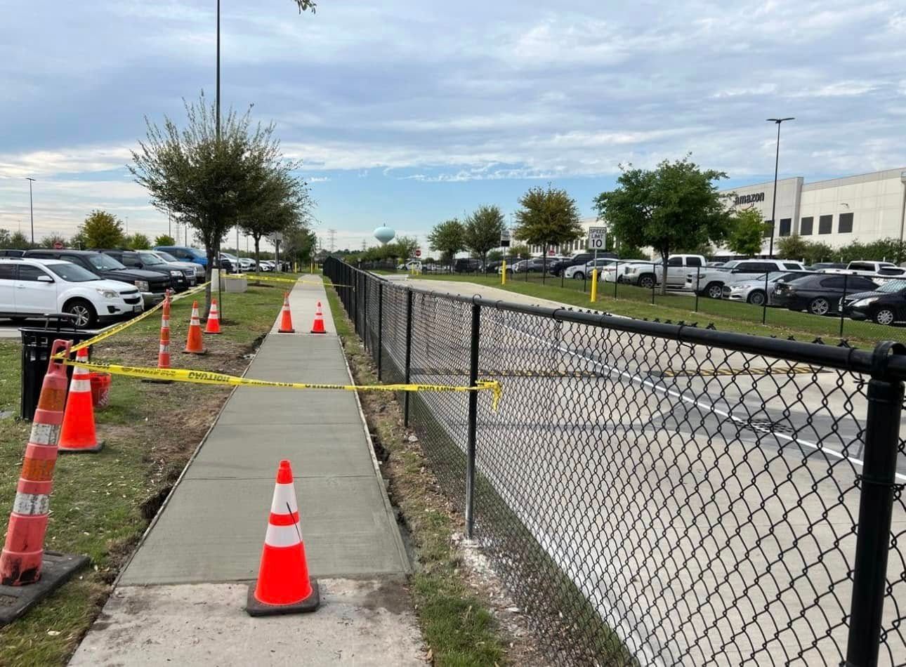 Sidewalk closed for construction with orange cones, caution tape, and a black chain-link fence.