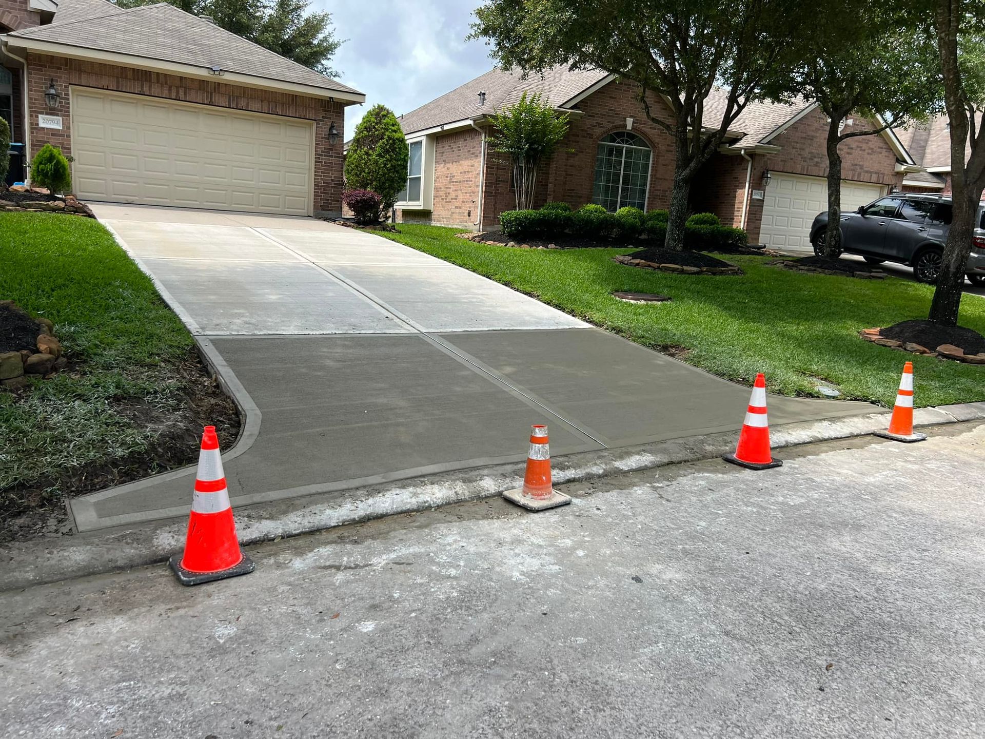 Newly poured concrete driveway with orange cones. Houses in background.