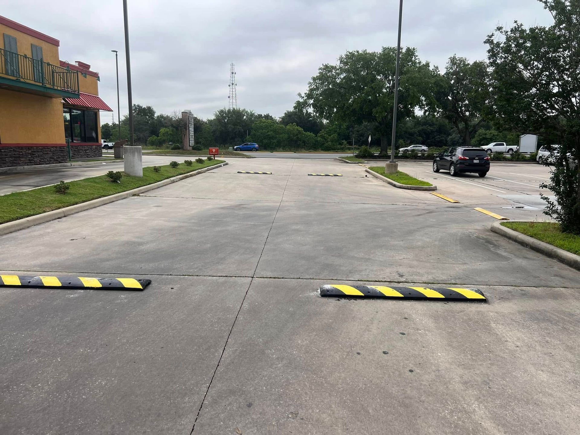 Parking lot with speed bumps, a car, and a restaurant under an overcast sky.
