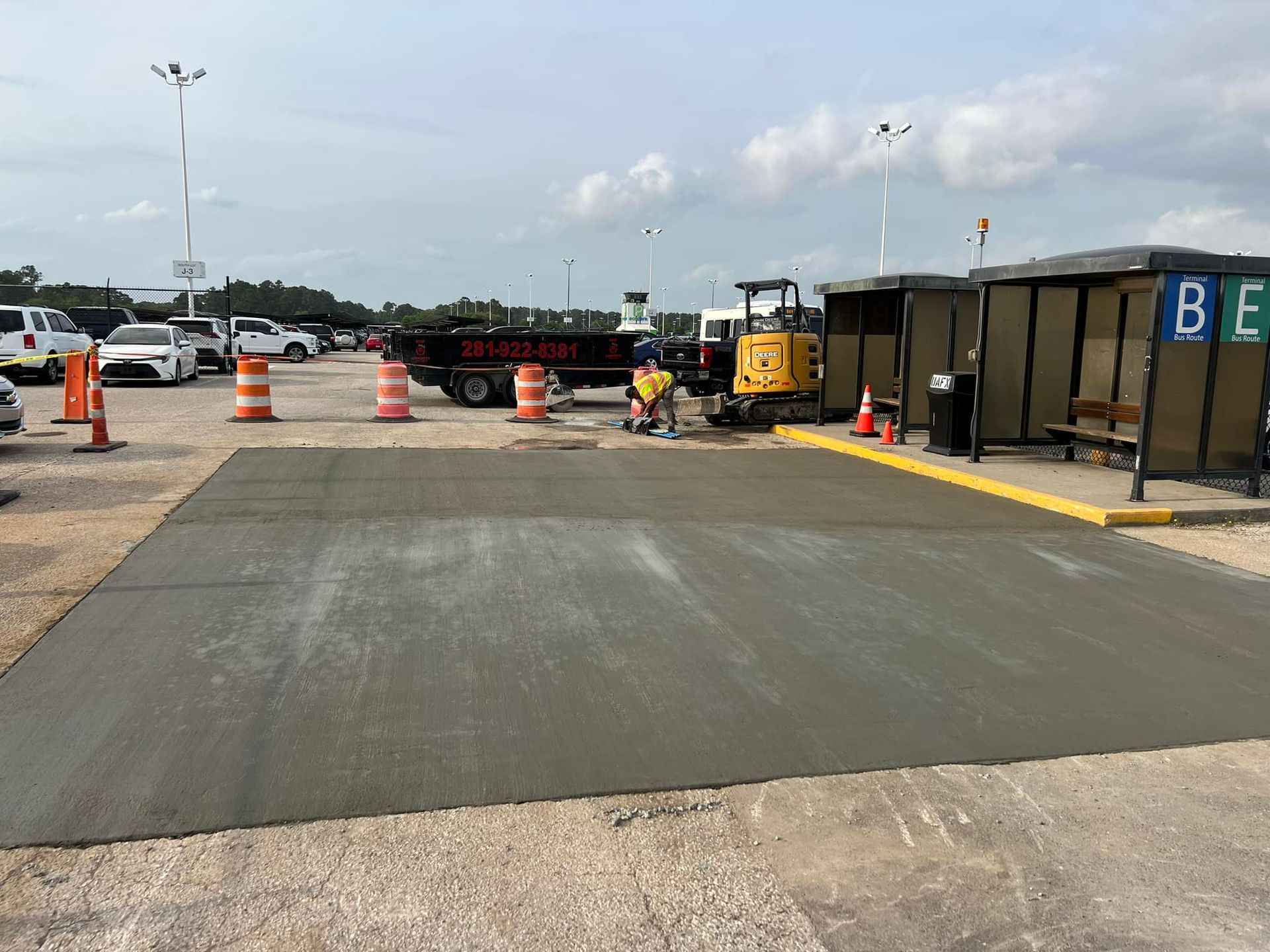 Concrete work in progress at a bus stop area; workers, orange cones, and equipment present.