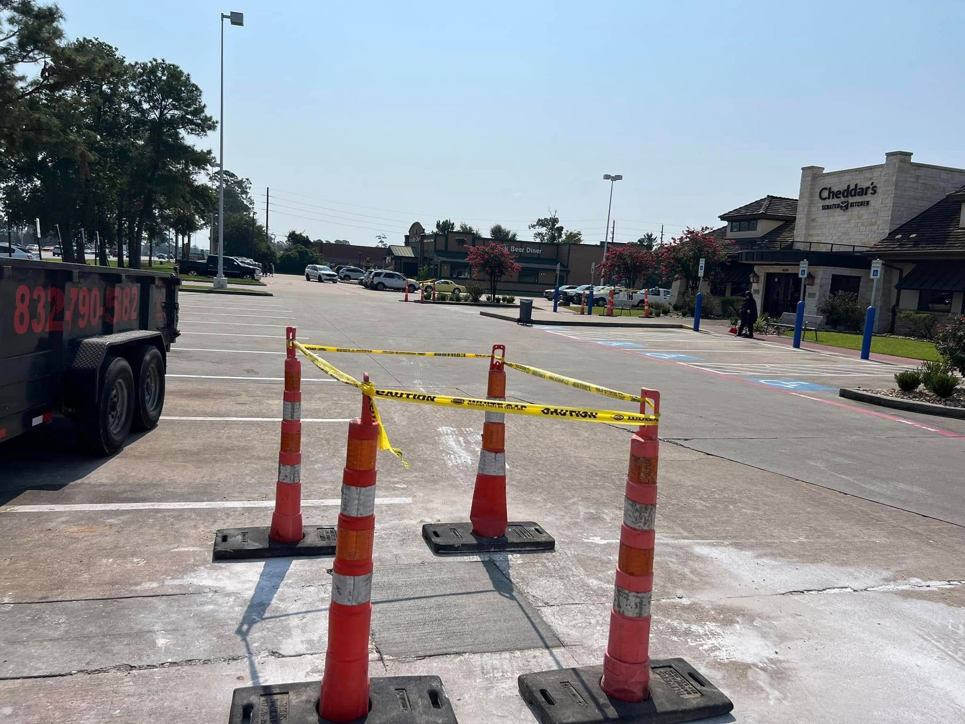 Orange cones with caution tape block parking lot area, near a restaurant, and trailer.