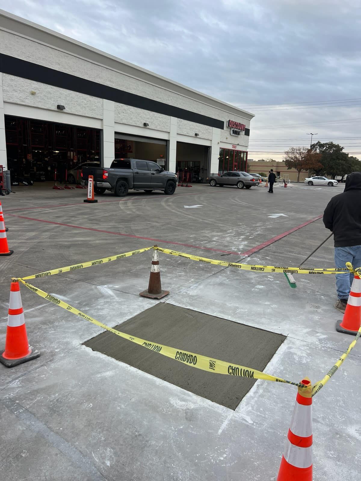 New concrete patch in front of auto repair shop, marked off with tape and cones.