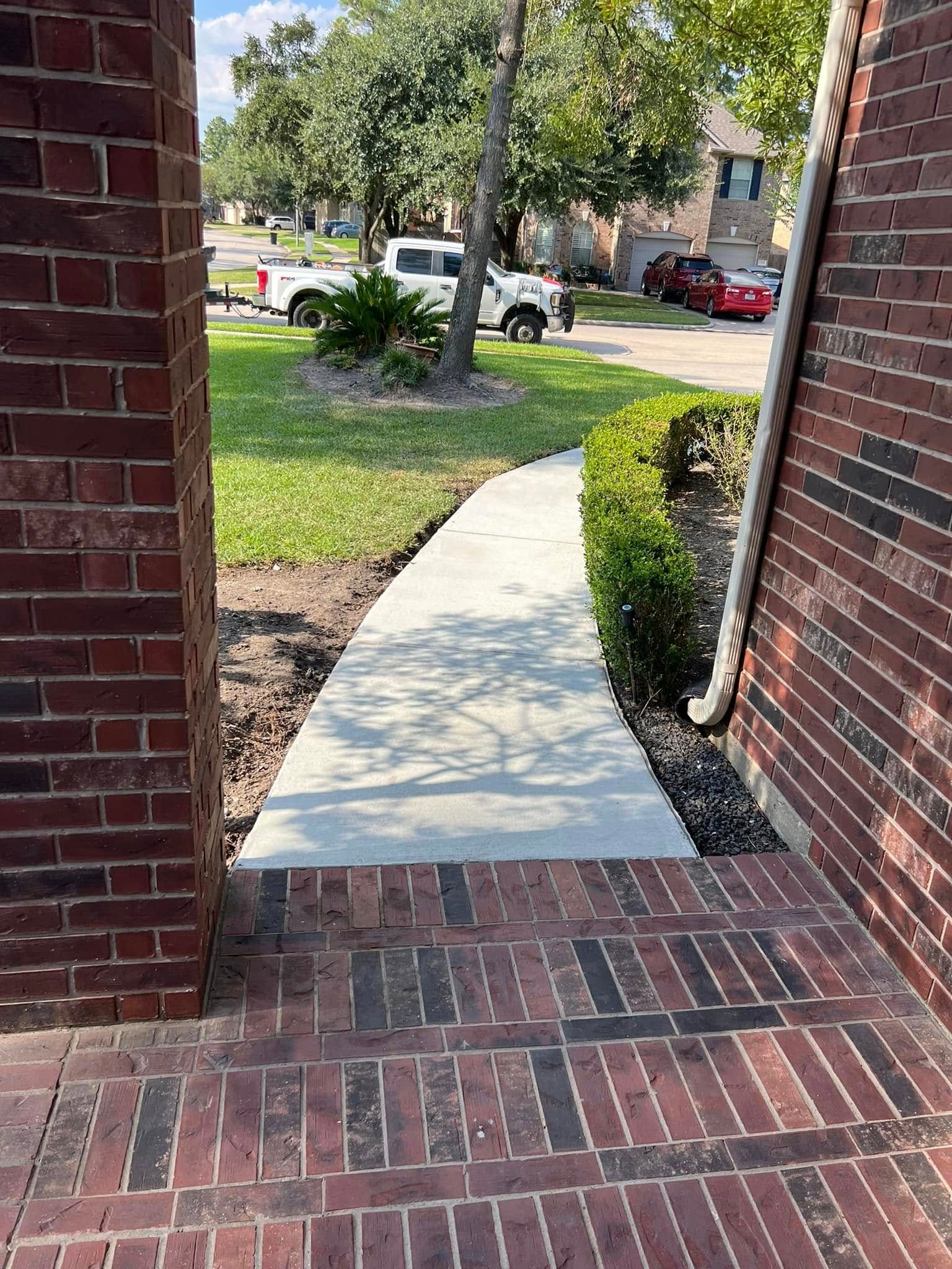Brick columns frame a concrete walkway leading to a residential street with parked vehicles.
