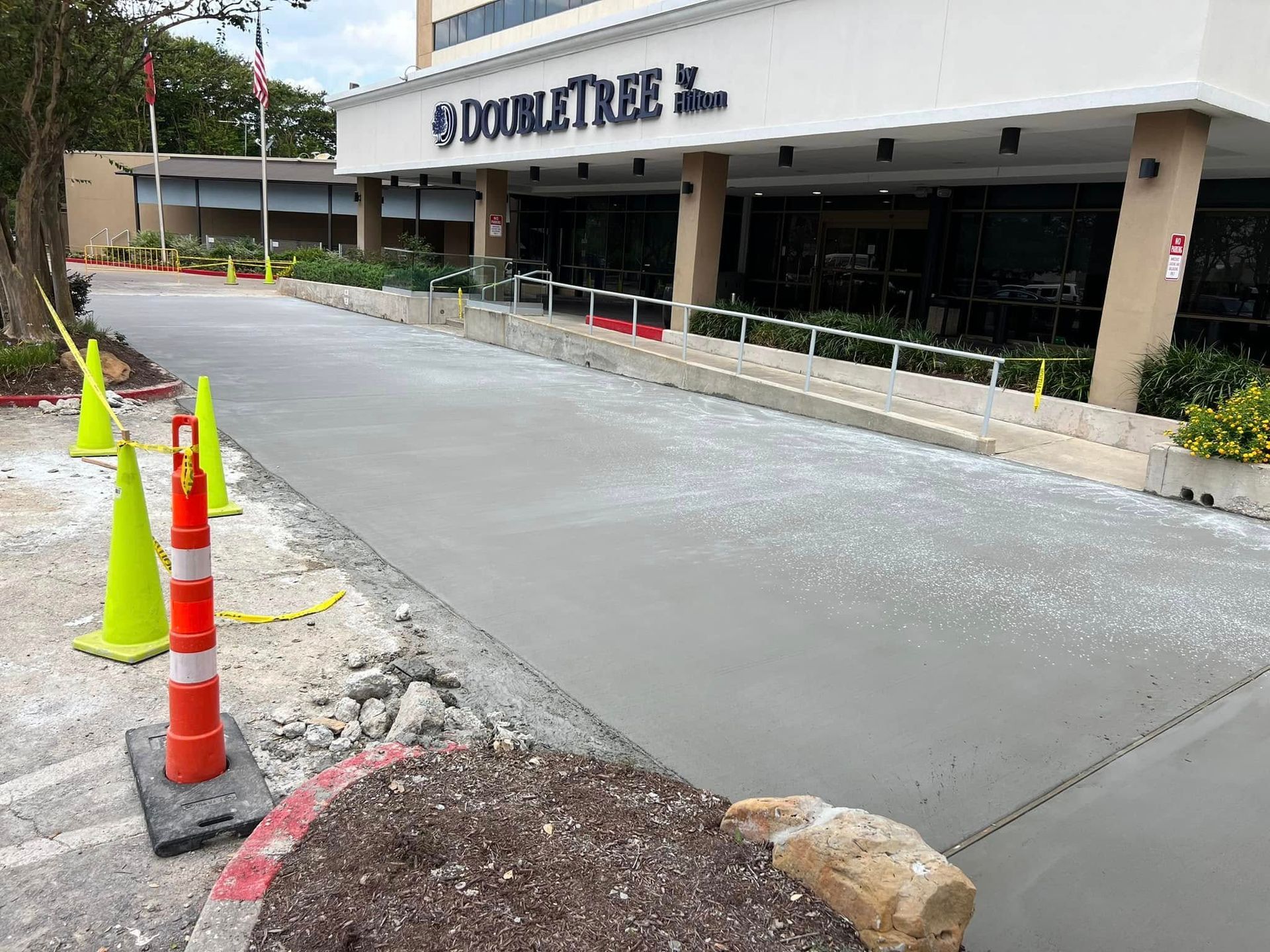 Newly poured concrete driveway in front of a DoubleTree hotel, with construction cones and caution tape.