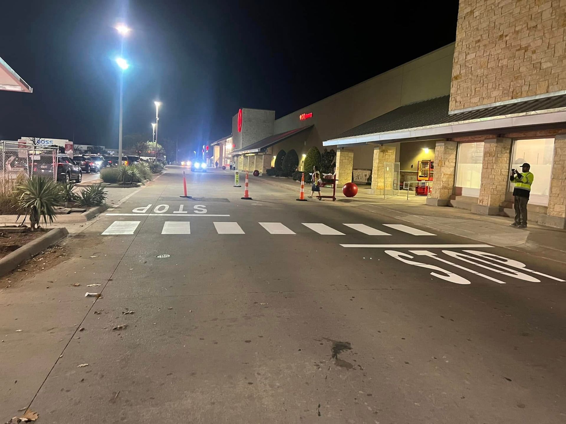 Nighttime view of a store with a crosswalk, traffic cones, and a security guard.