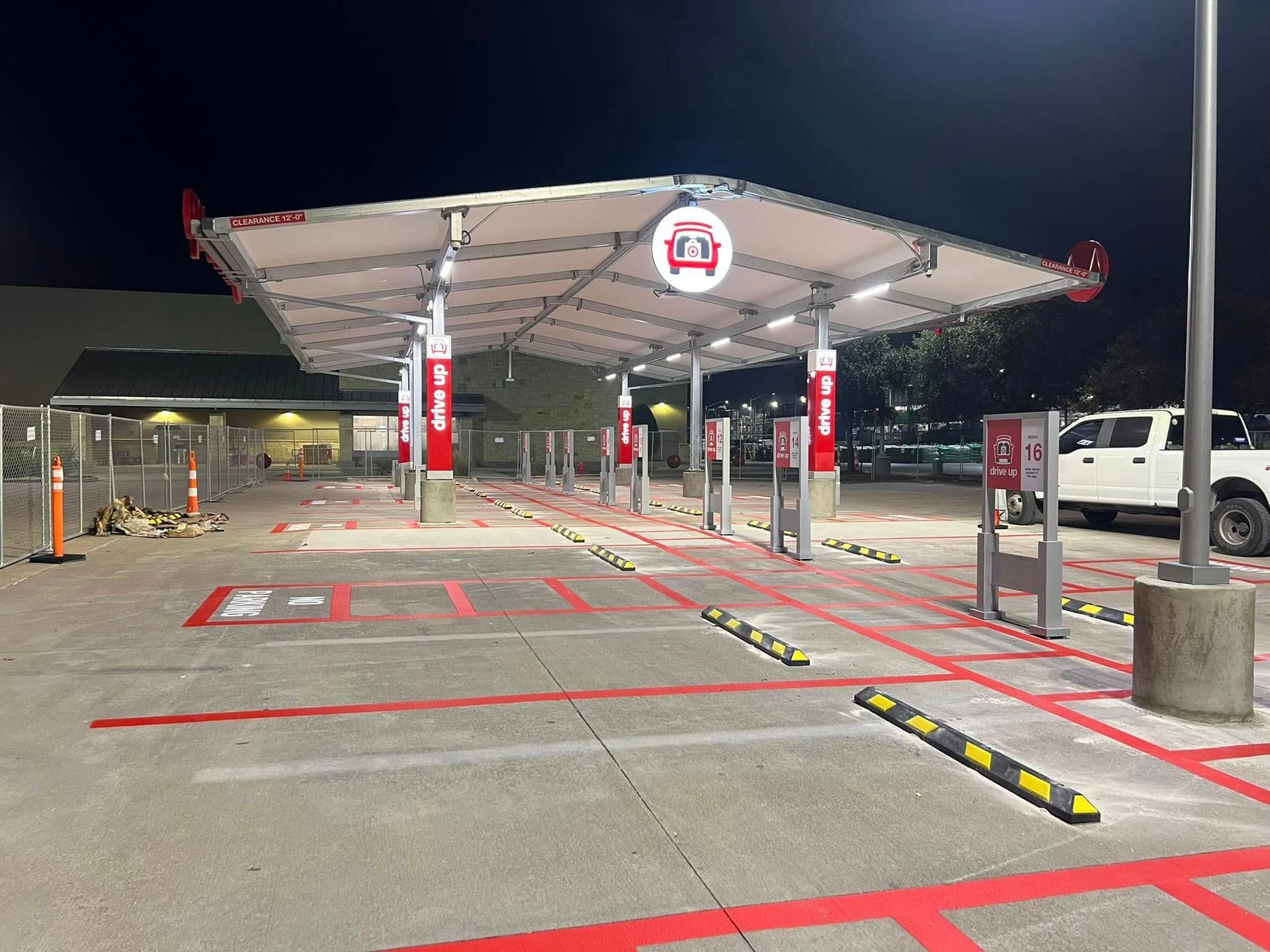 Drive-up area with charging stations, canopy, red and white accents, at night. Concrete ground with painted parking lines.