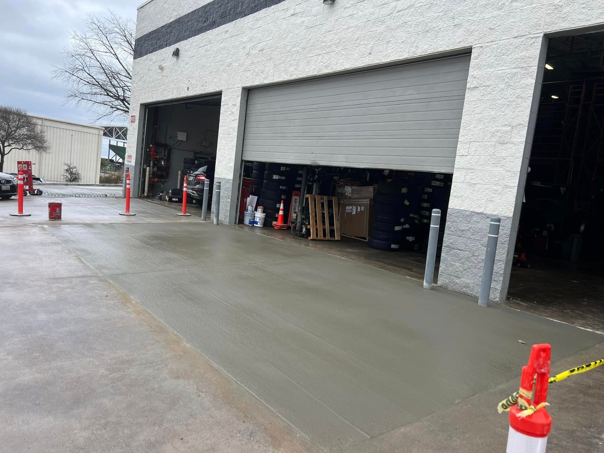 Newly poured concrete driveway in front of a commercial building with garage doors. Safety cones and caution tape.