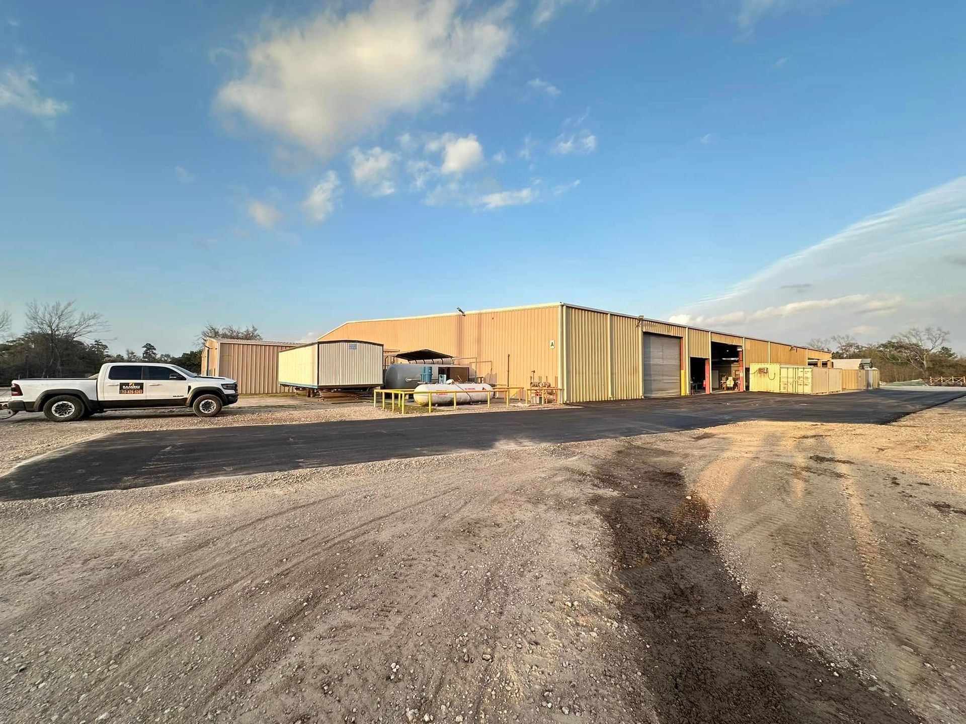 A tan industrial building with a truck parked in front, under a blue sky with clouds.