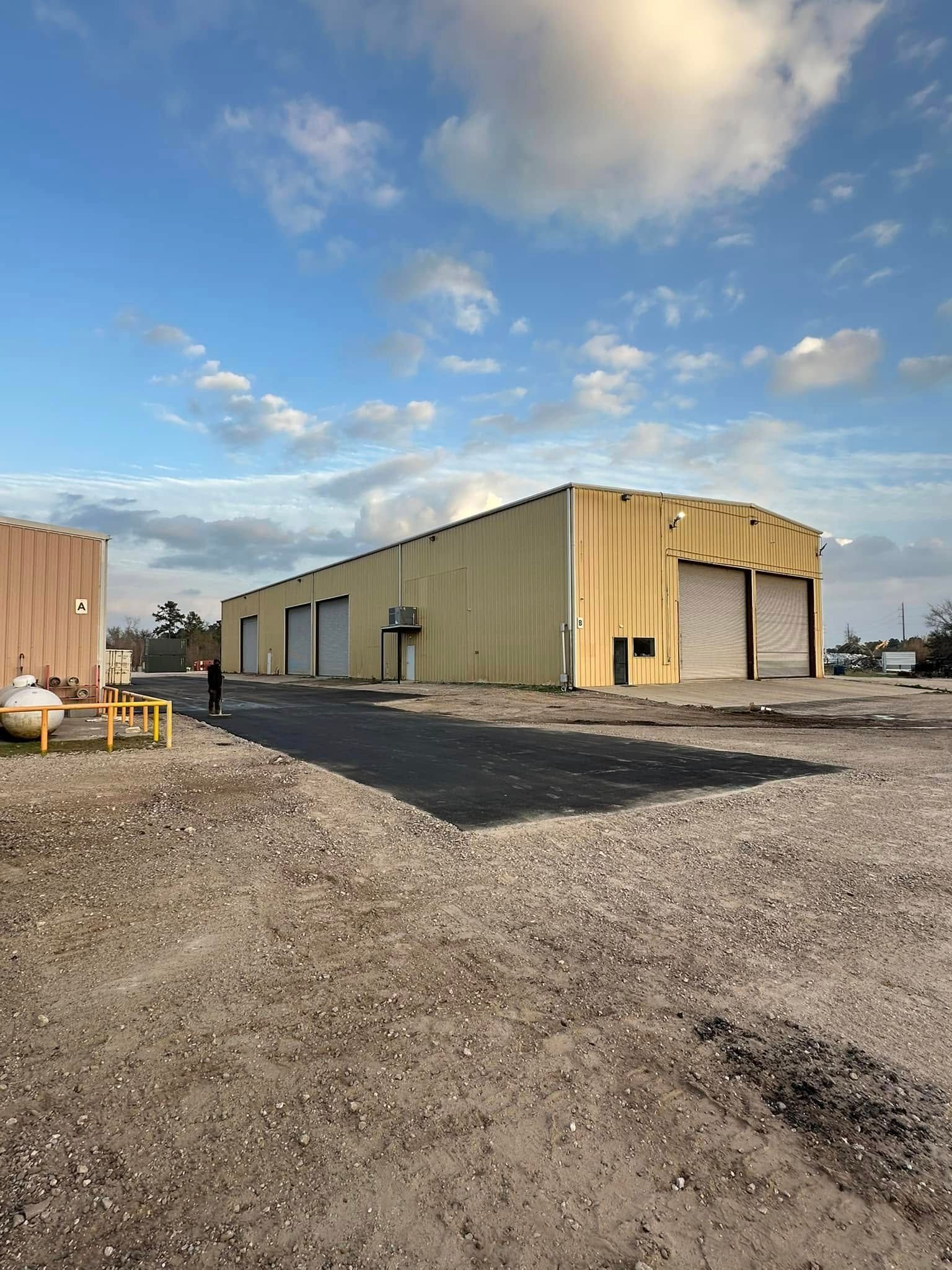 Yellow warehouse with several closed roll-up doors, on a gravel lot under a partly cloudy sky.