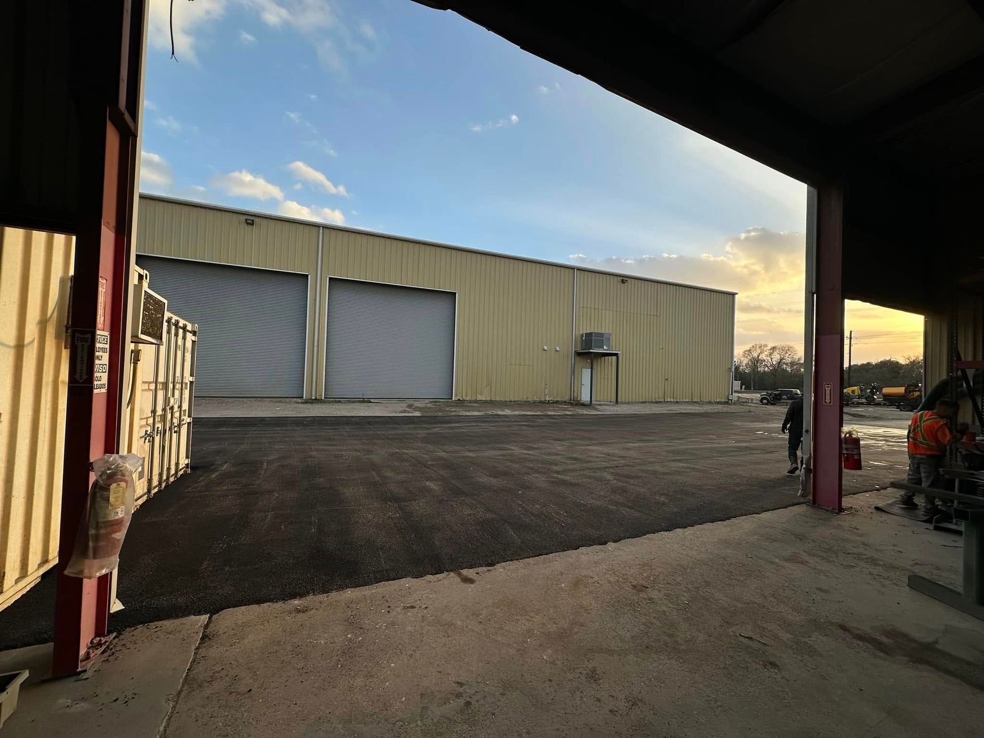 A warehouse with two roller doors, viewed from a covered area, with a person walking.