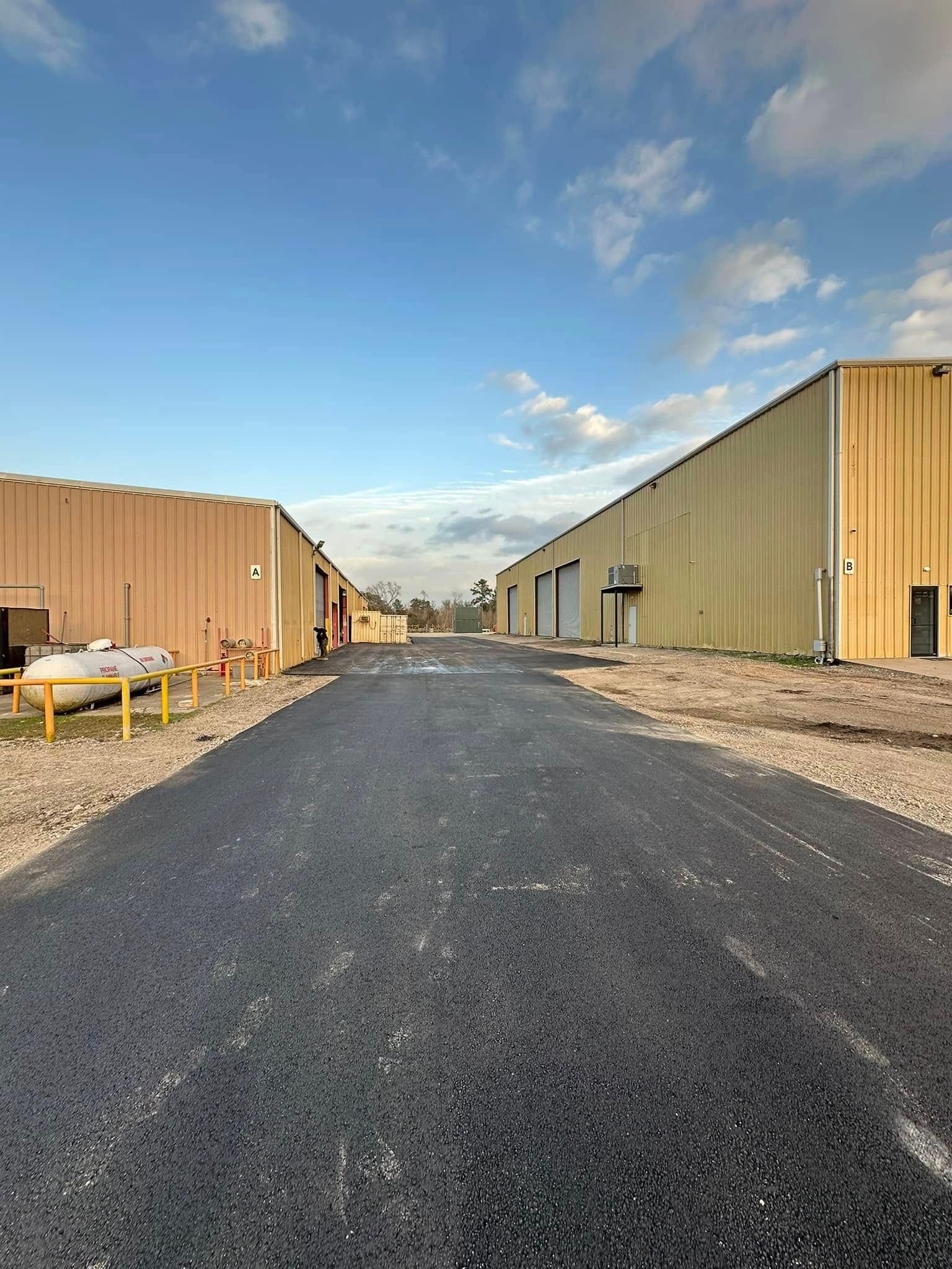 Paved road between two industrial buildings under a cloudy blue sky.