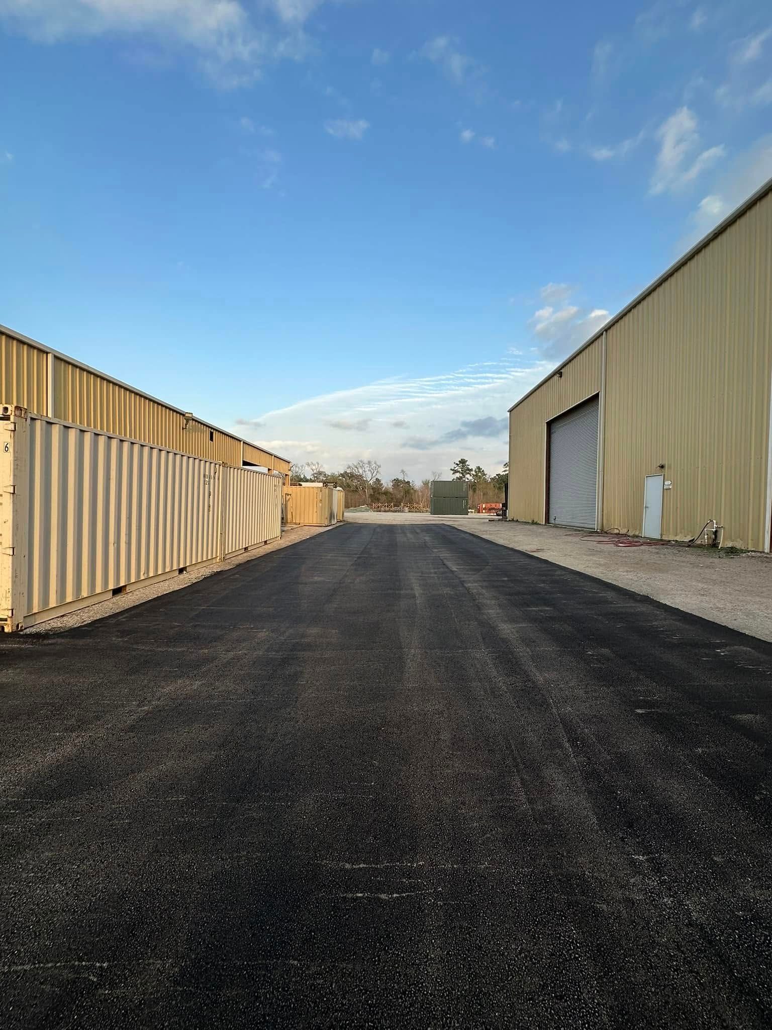Asphalt road between two tan industrial buildings under a blue sky.