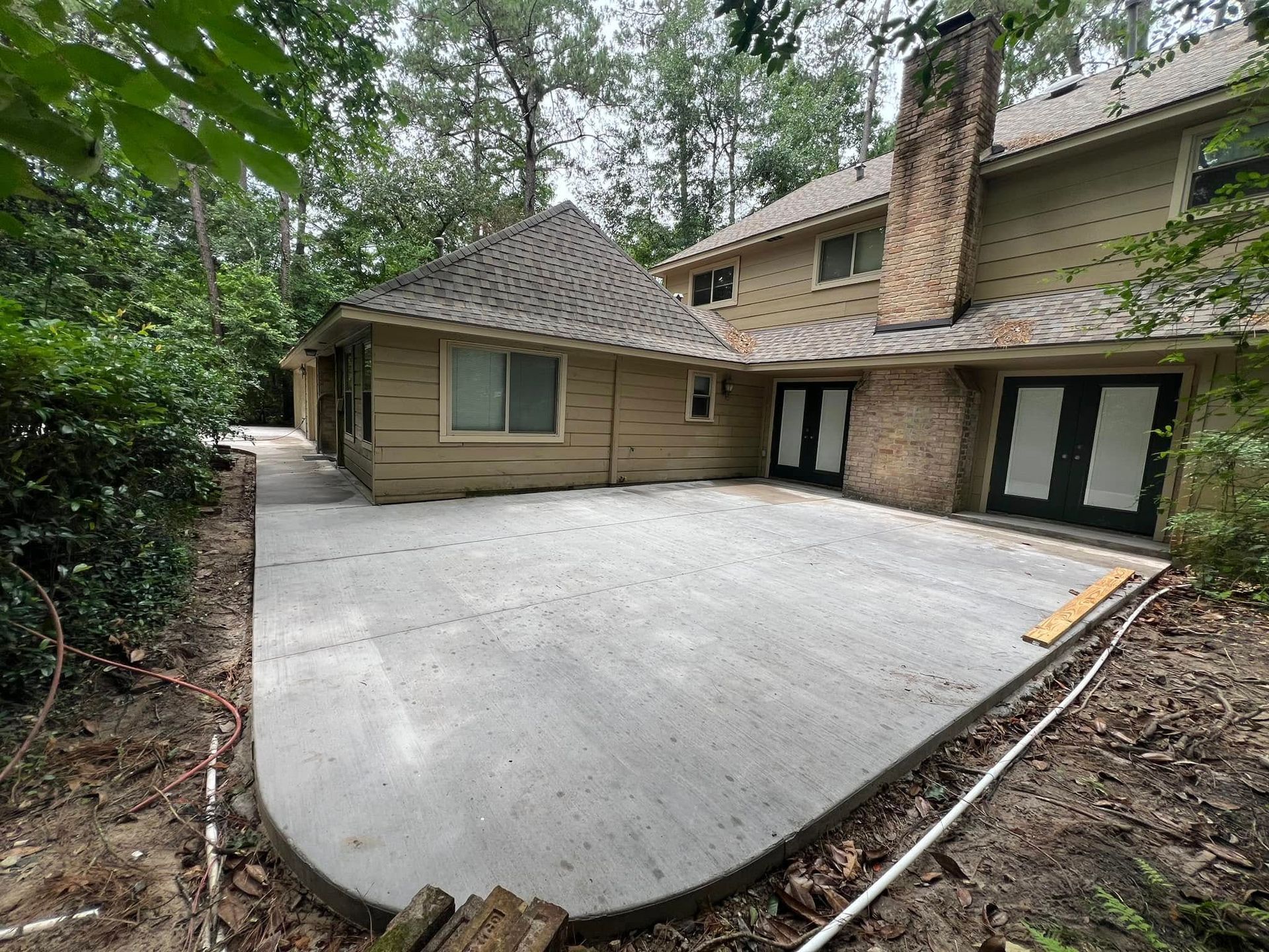 New concrete patio next to a two-story beige house with a brick chimney and black double doors.
