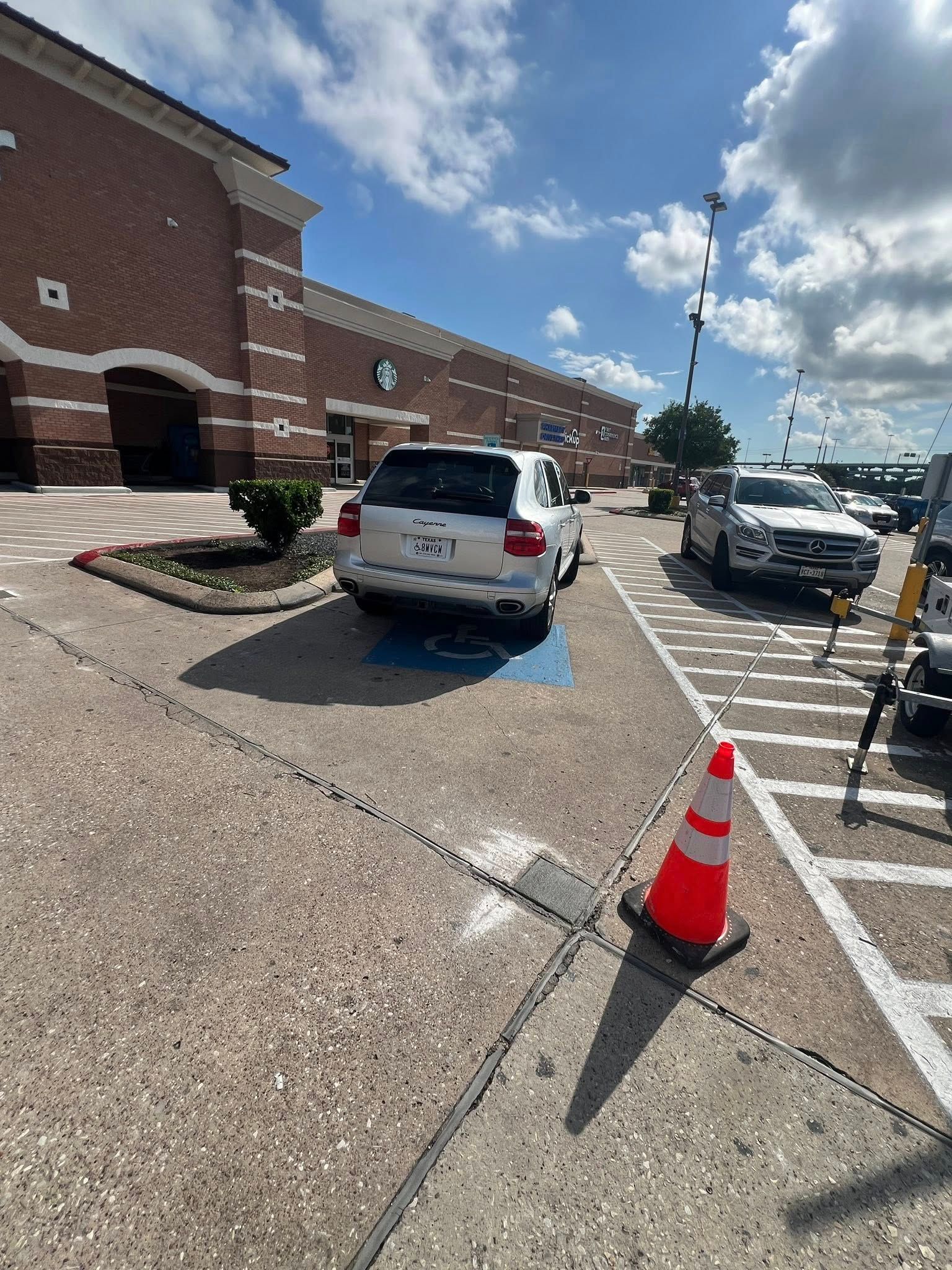 White SUV parked in handicap spot outside a brick building under a sunny sky.